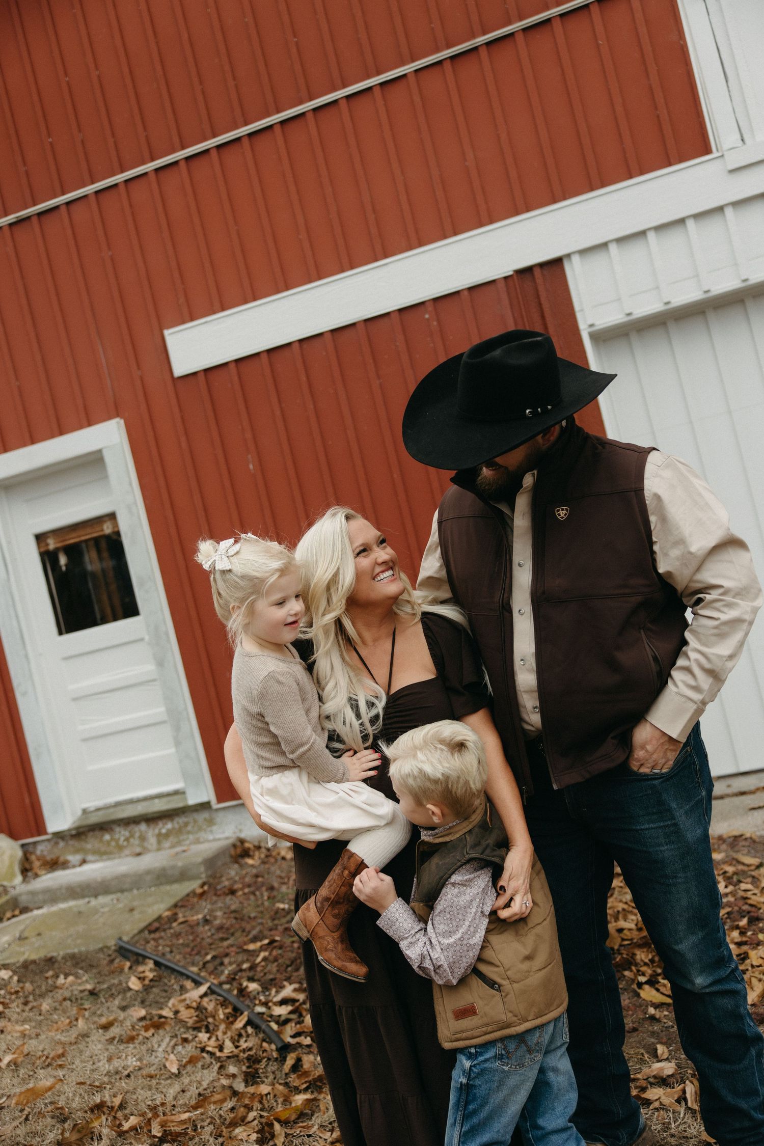 A group stands together outside a rustic red barn with white trim on an autumn day.