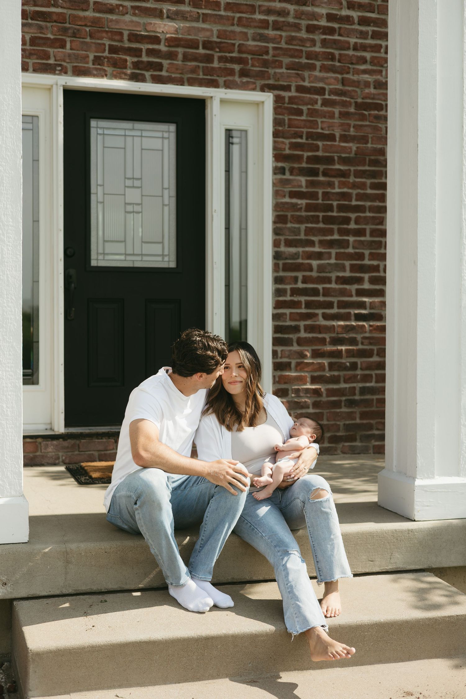 A couple sits barefoot on a porch step in front of a brick building with white columns and black doors.