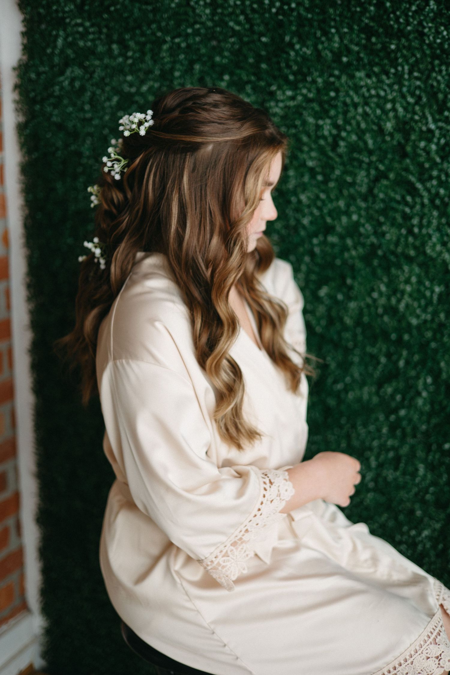 Side view of woman in white robe with baby's breath flowers in her hair against green backdrop.