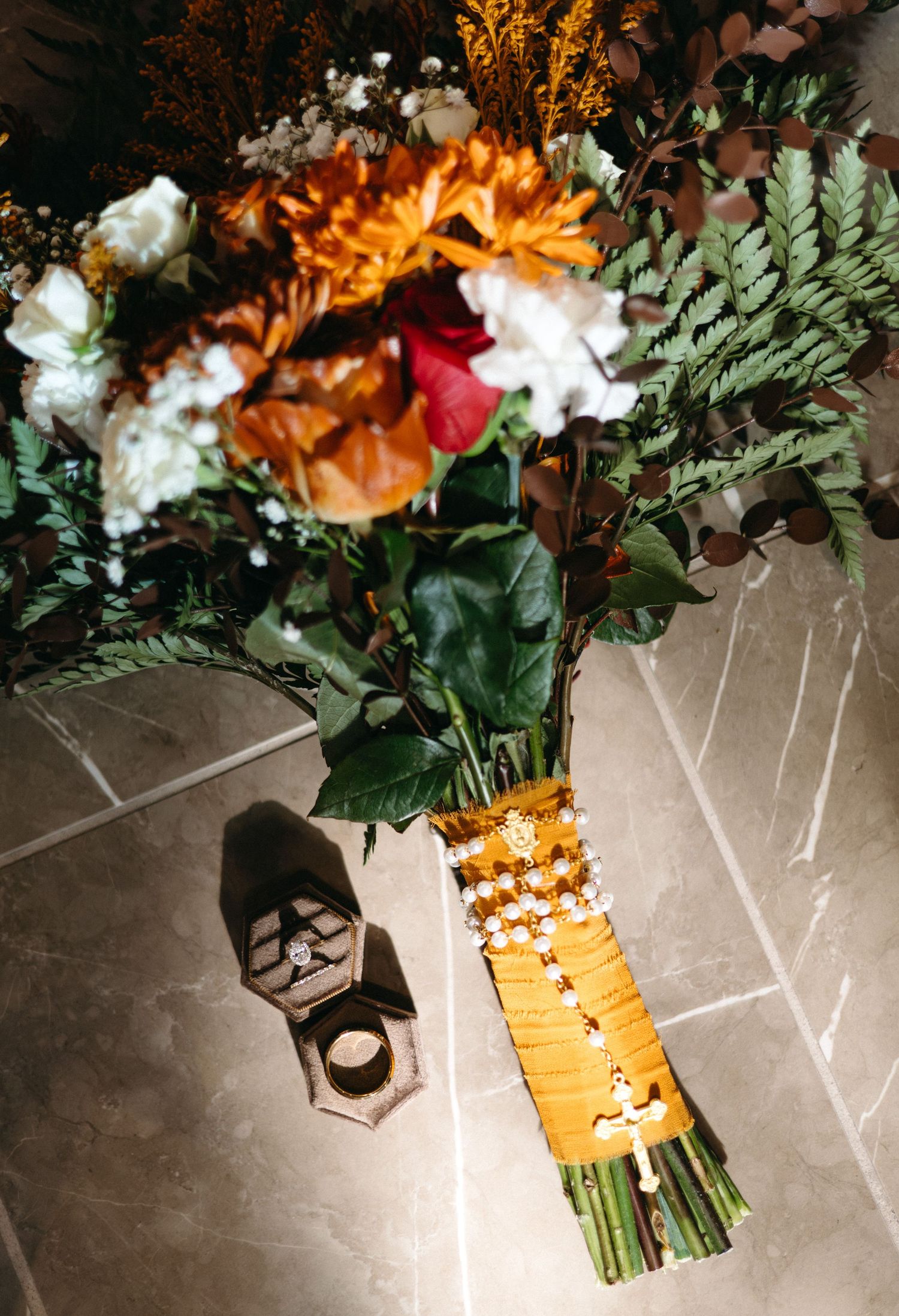 A wedding bouquet with orange and white flowers wrapped in gold ribbon casting a shadow on a stone floor.