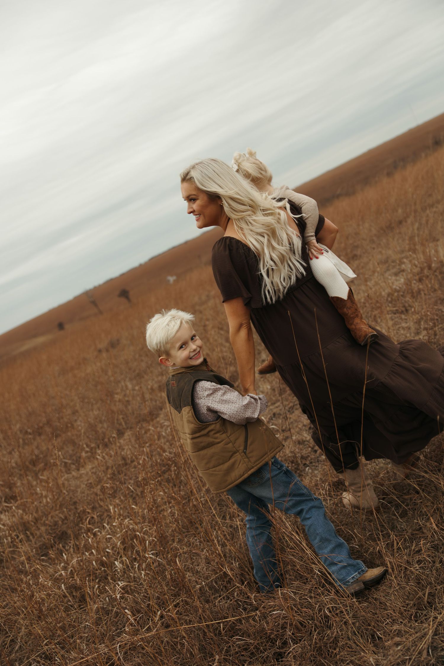 Two people in warm clothing share a playful moment together in a brown autumn field under an overcast sky.