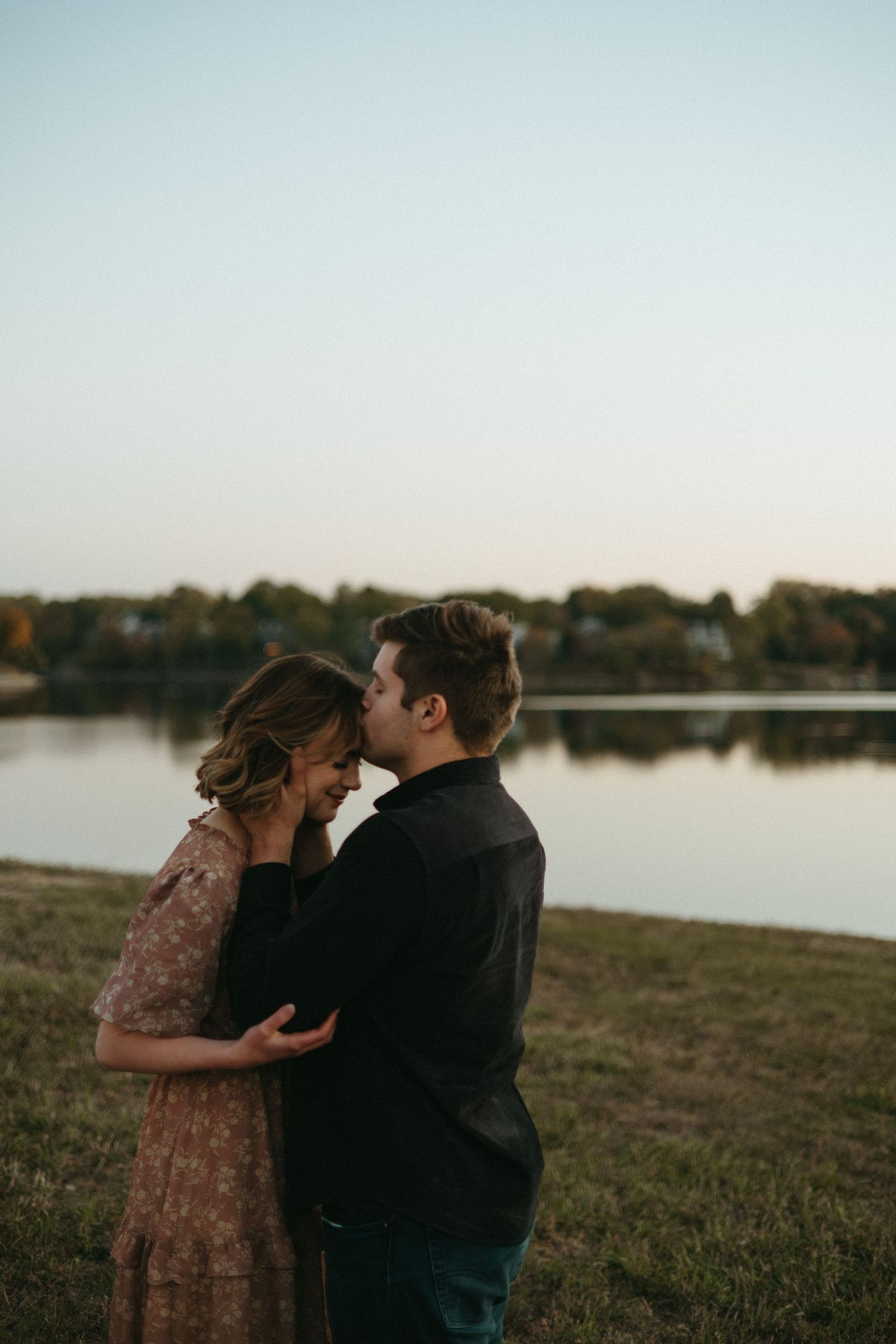 A tender moment between a couple by the lake during sunset.