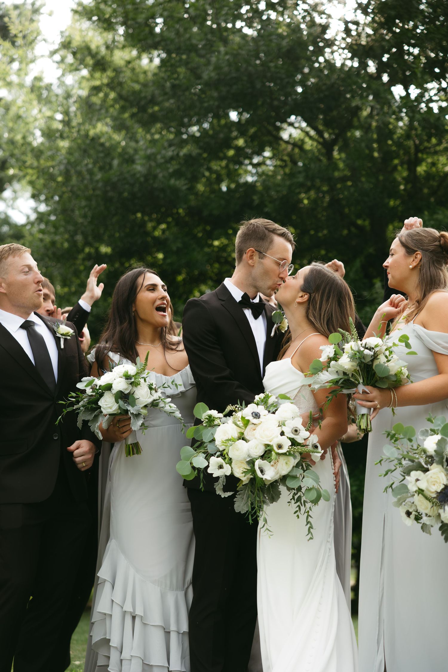 Wedding party laughing together outdoors while holding elegant white floral bouquets.