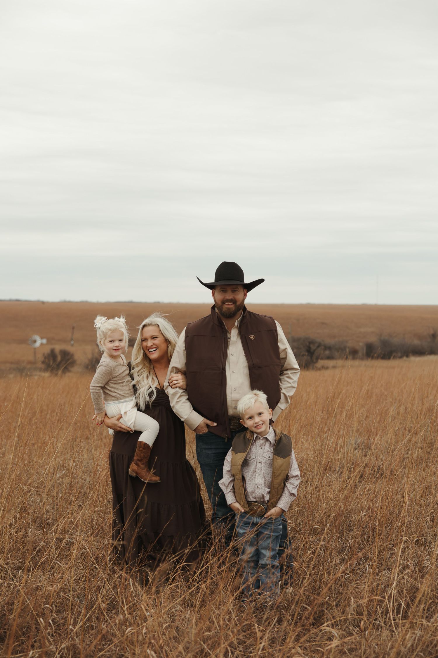 A family stands together in a golden autumn field wearing western-inspired clothing at sunset.