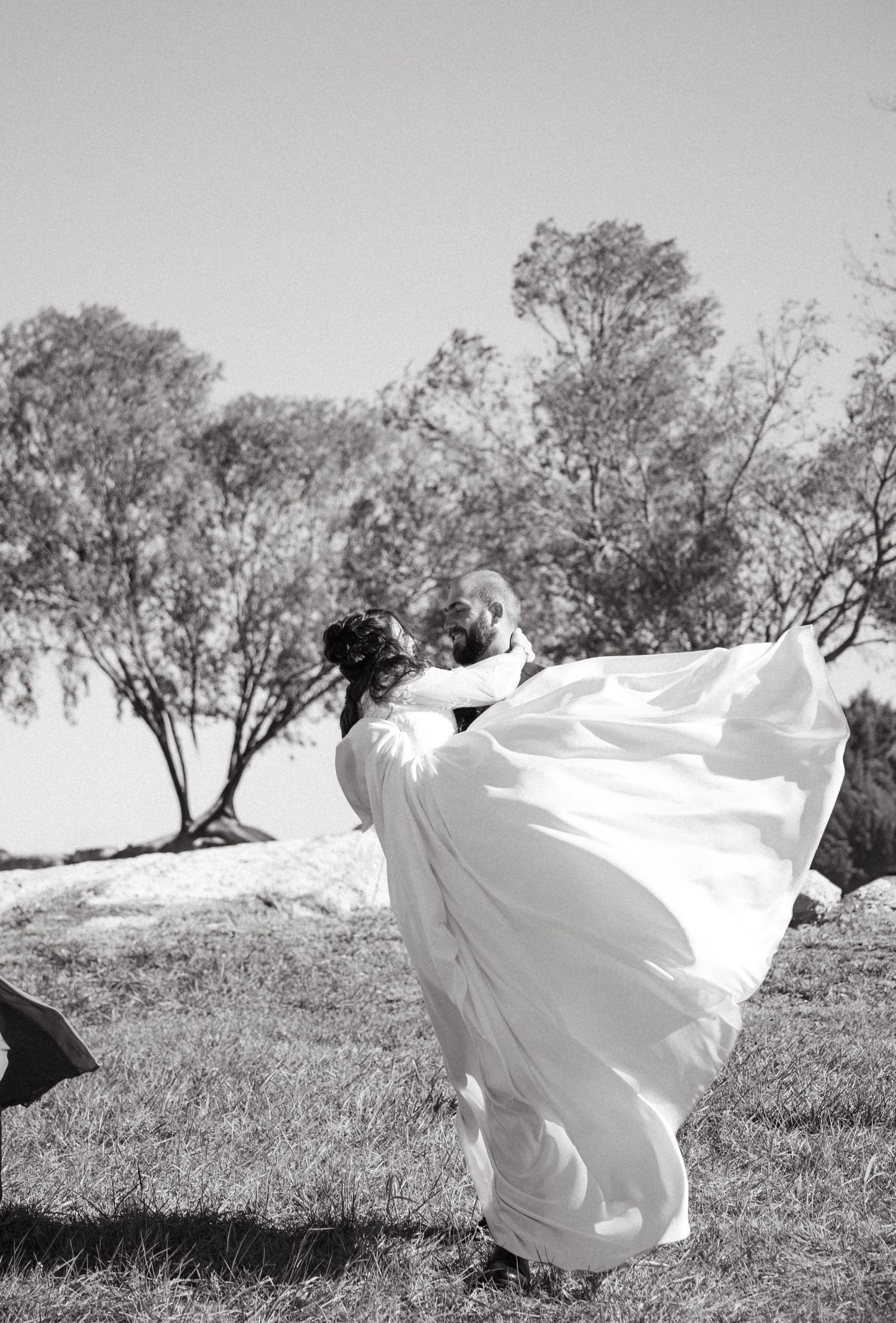 A flowing white fabric billows dramatically across a grassy field with trees in the background creating an ethereal scene.