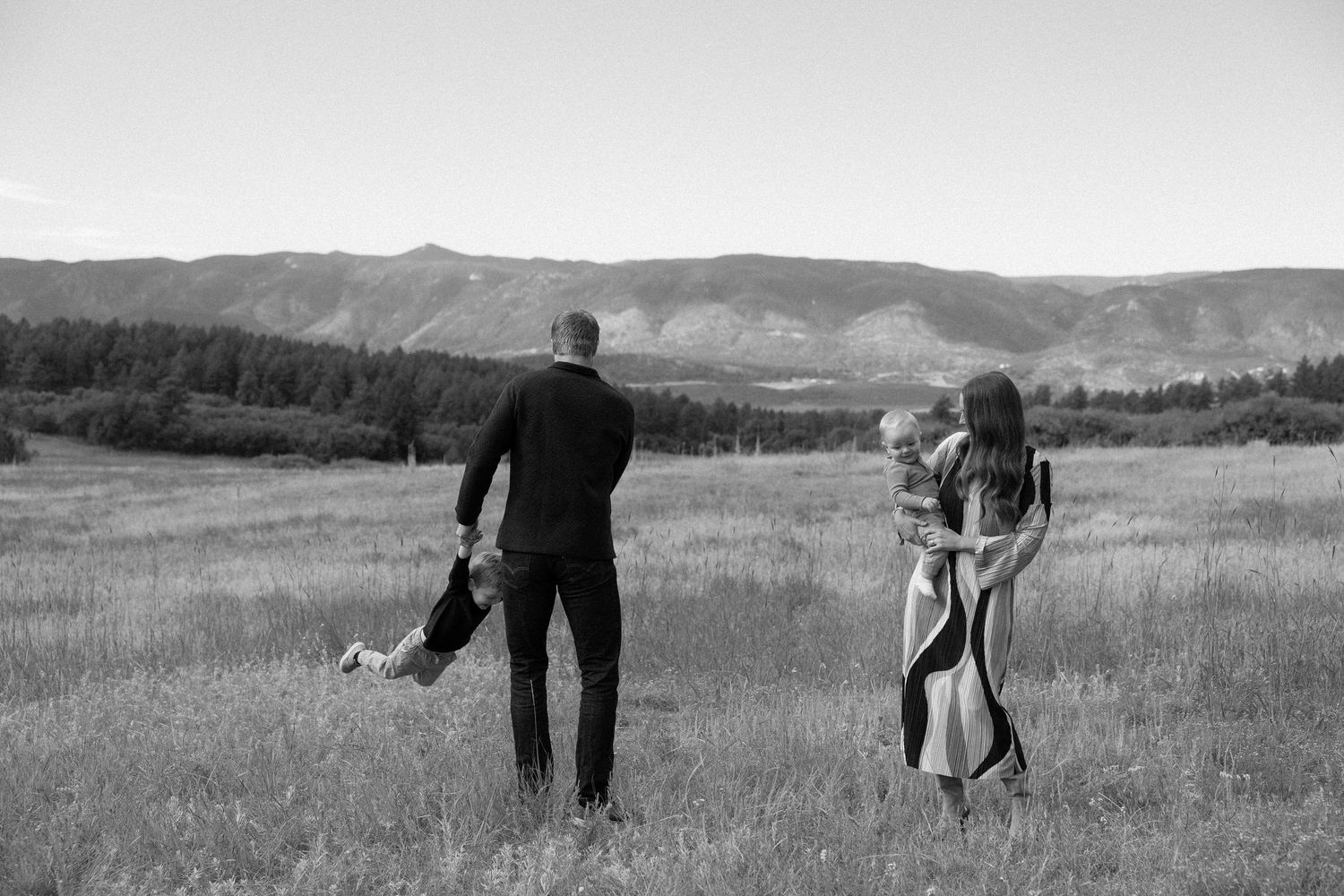 A couple with their dog enjoy a peaceful moment in a scenic mountain meadow captured in black and white.