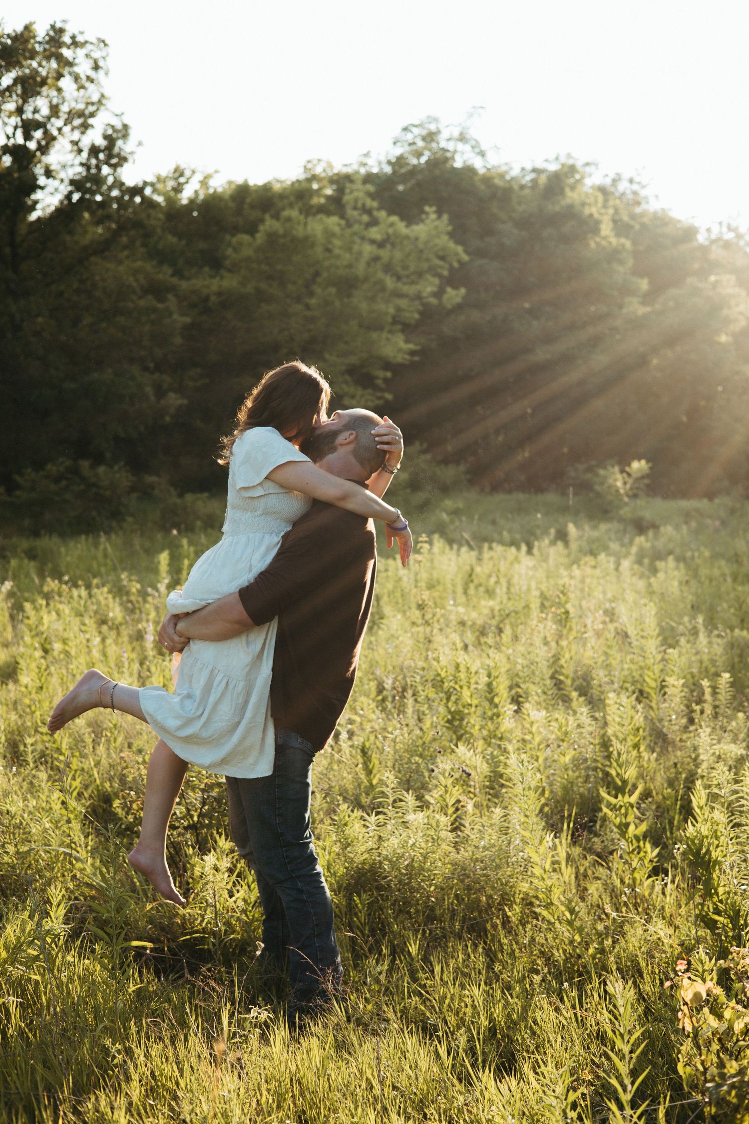 A couple embraces and spins together in a sunlit meadow during golden hour.