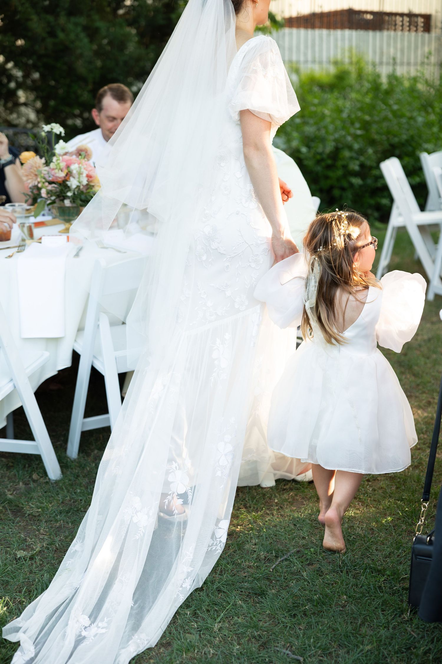 Wedding party dancing on grass with flowing white dresses.