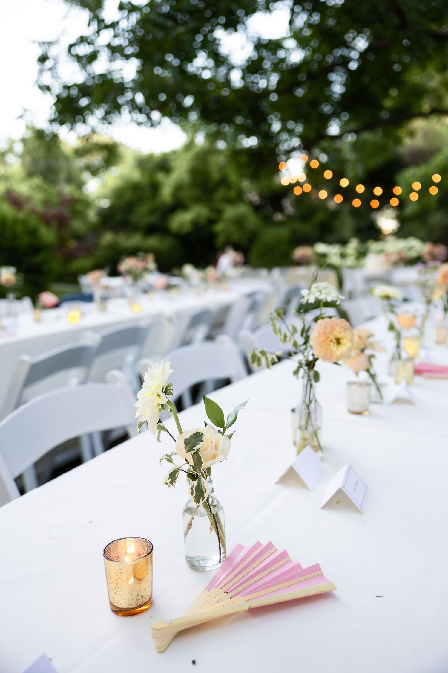 Outdoor wedding reception tables decorated with white linens, delicate floral centerpieces and string lights overhead.