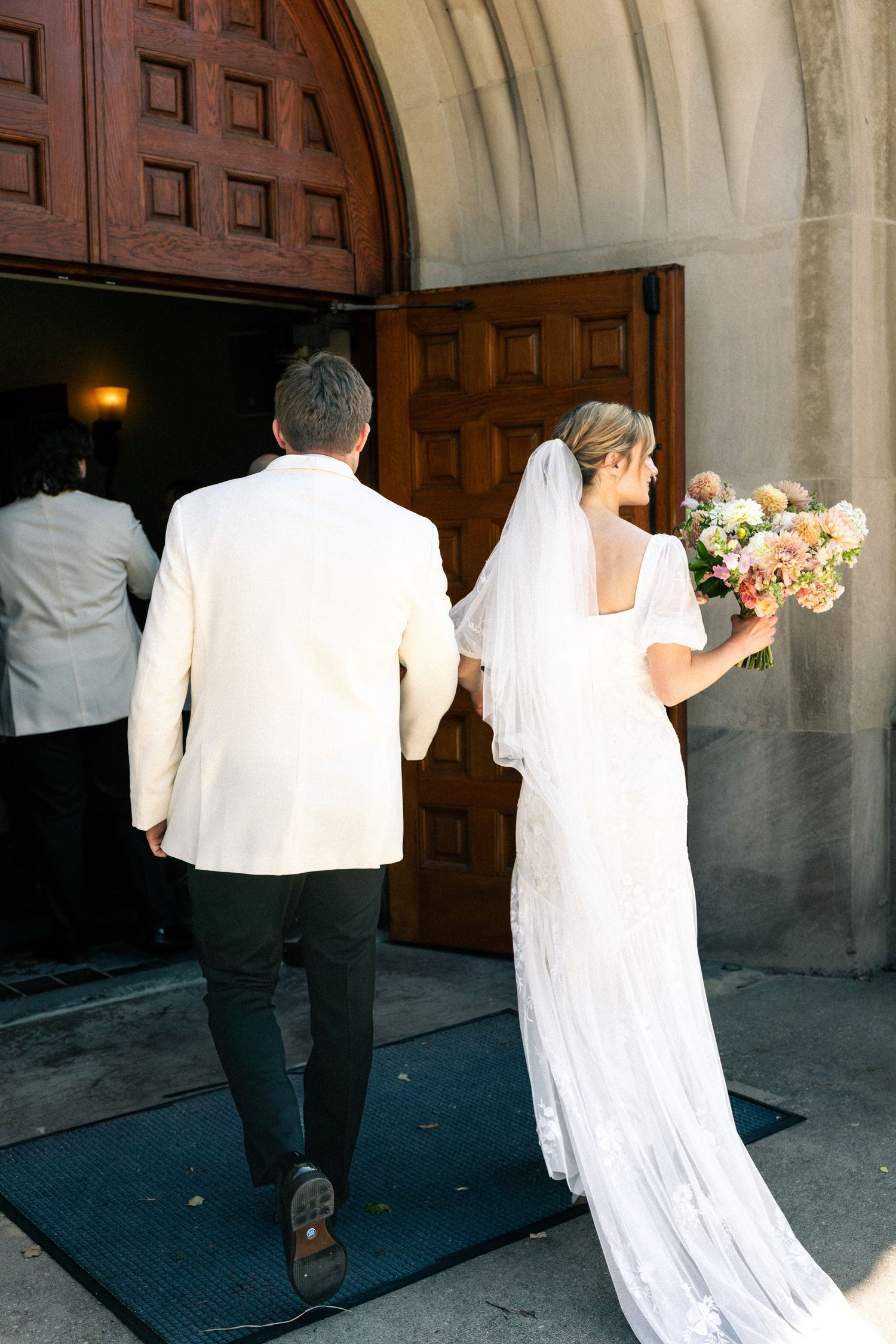 Wedding couple walking through ornate wooden church doors.