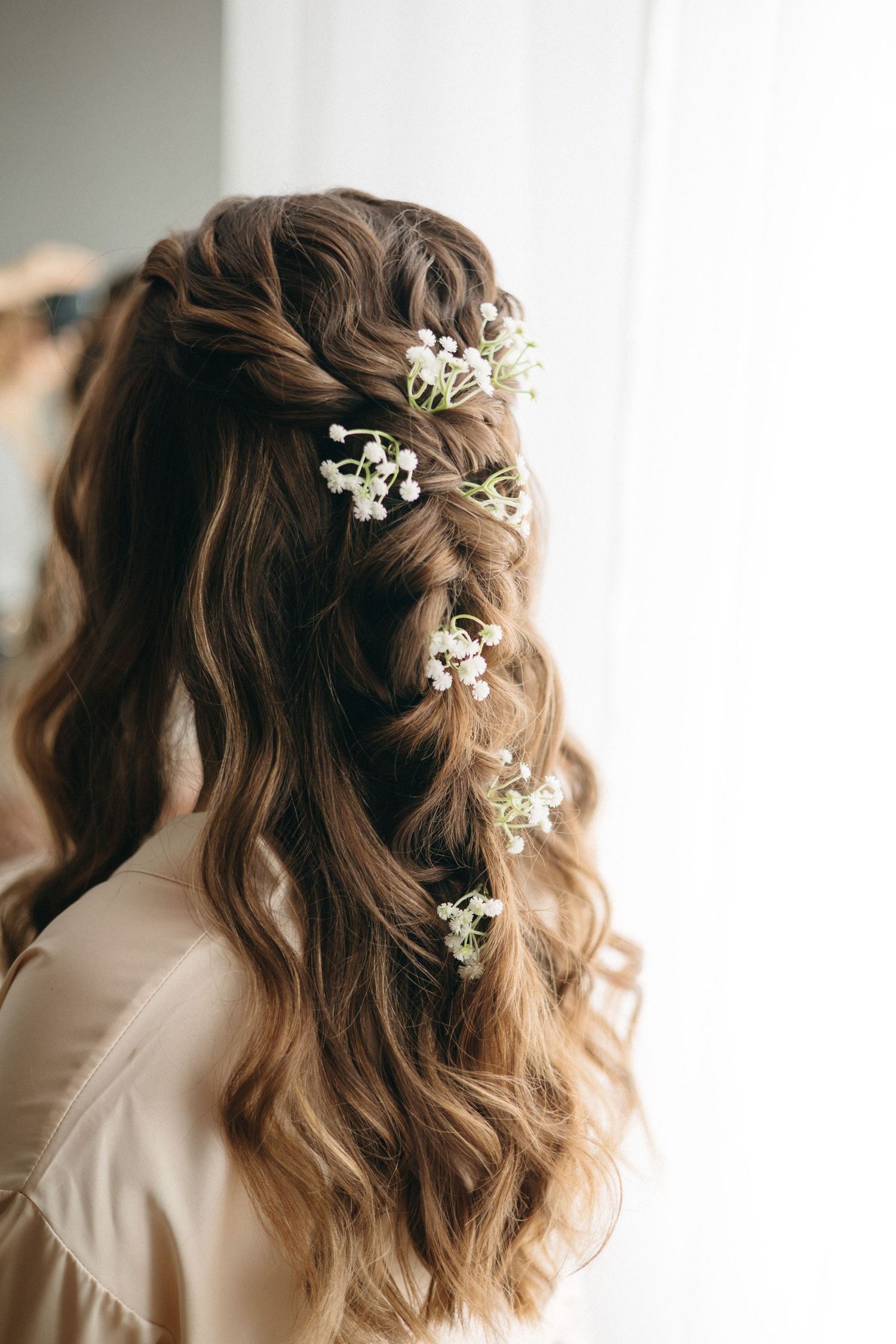 Close up of wavy brown hair styled with delicate baby's breath flowers.