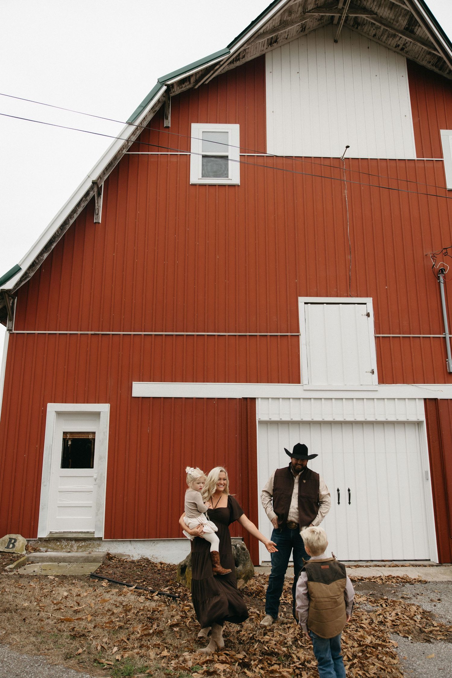 A family gathers in front of a classic red barn with white trim on an autumn day.