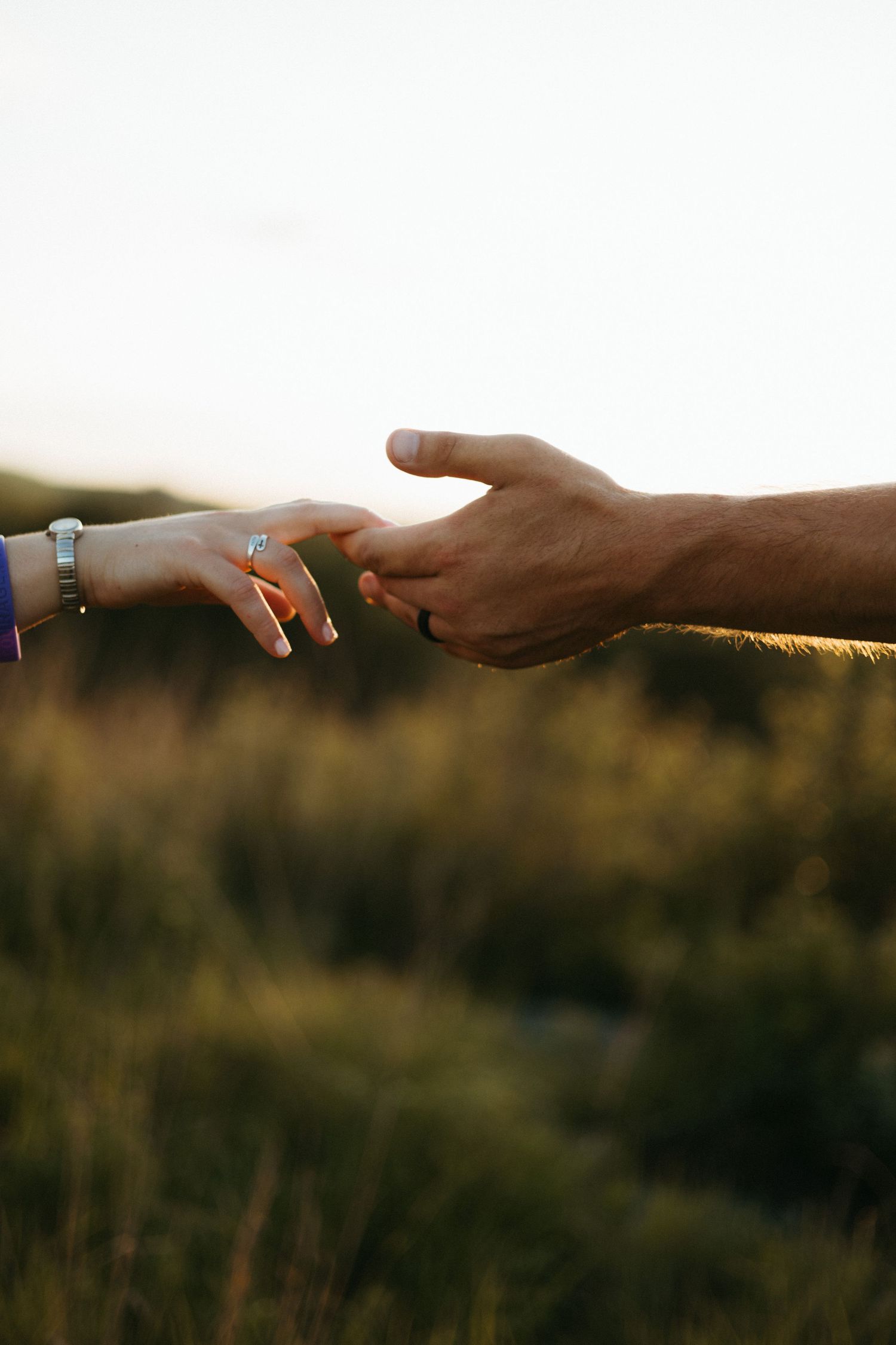 Close-up of hands reaching to touch in golden sunlight with jewelry details.