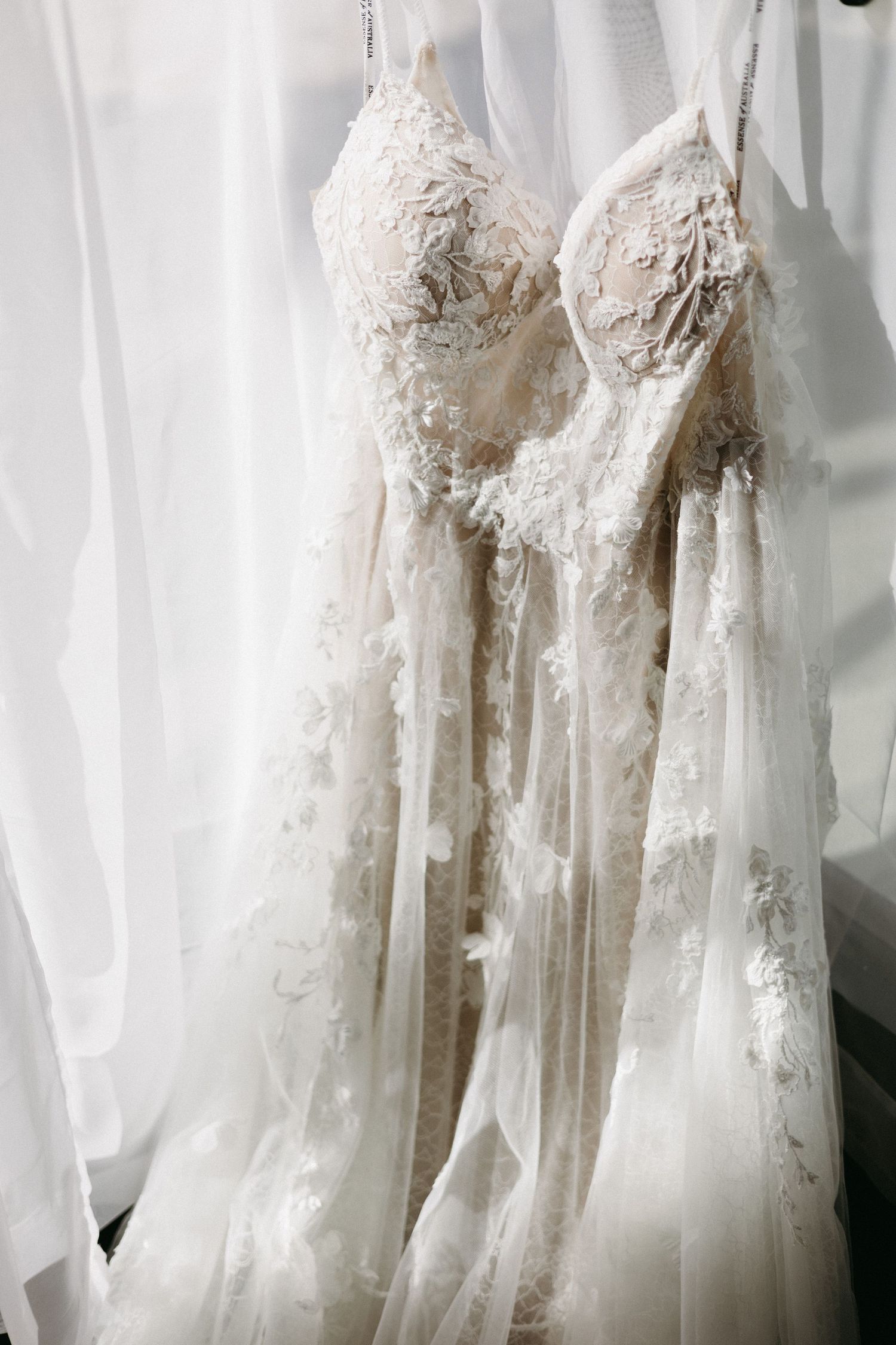 Row of elegant white lace wedding dresses hanging against a light background.
