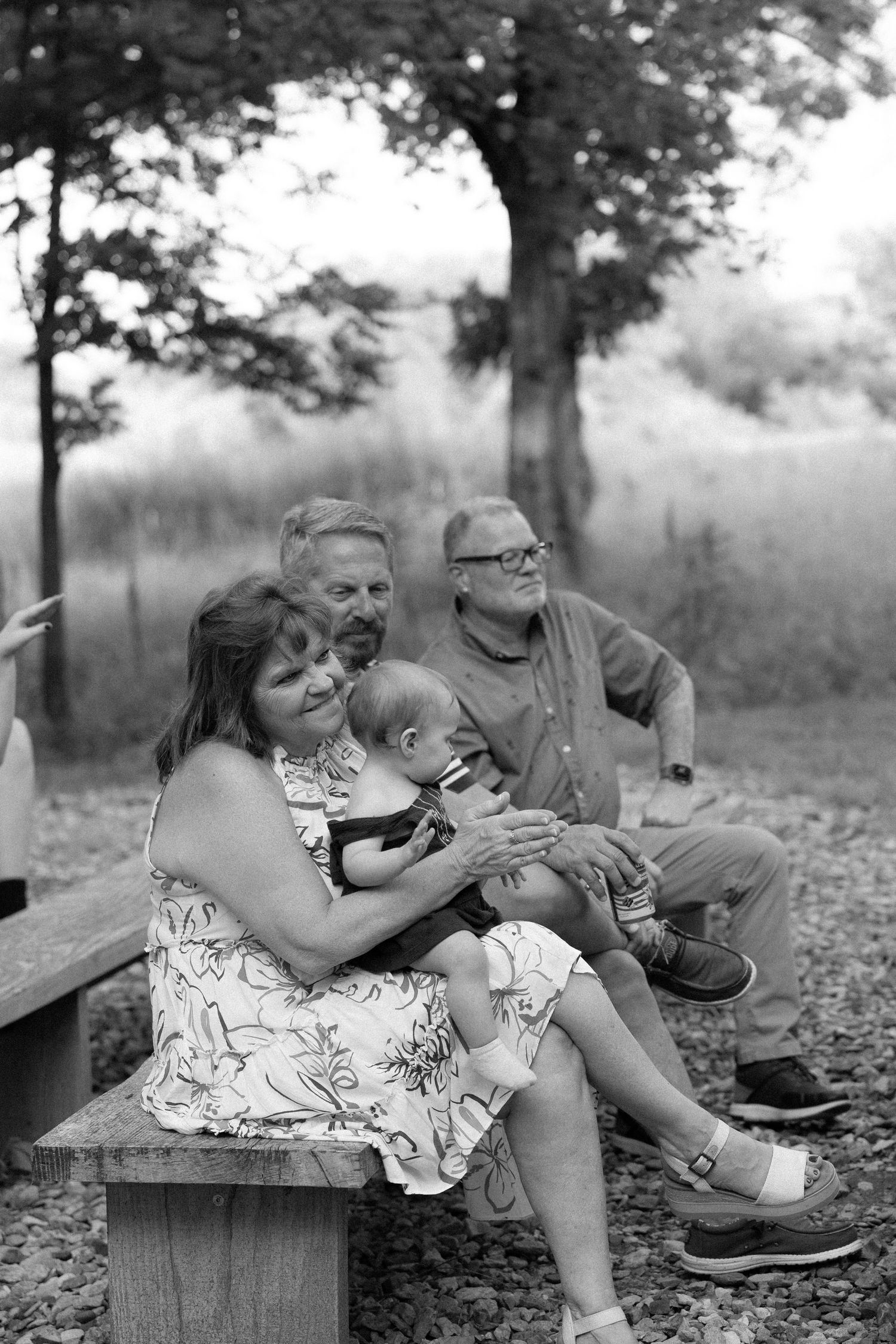 A tender family moment captured in black and white on a wooden bench outdoors.