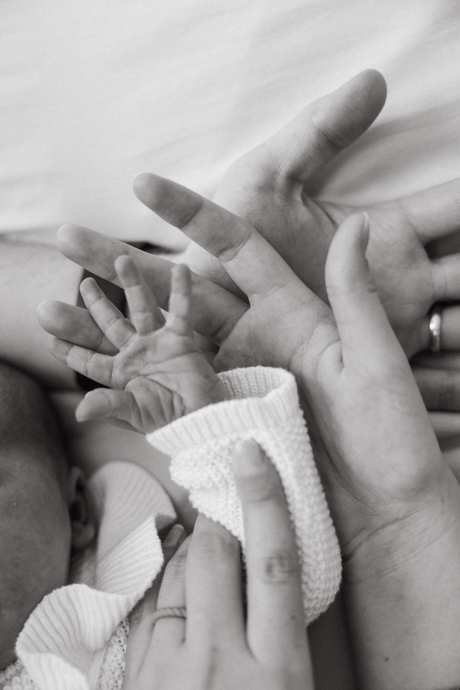 Black and white sequence of hands holding and caressing a newborn baby's tiny fingers wearing white knit clothing.