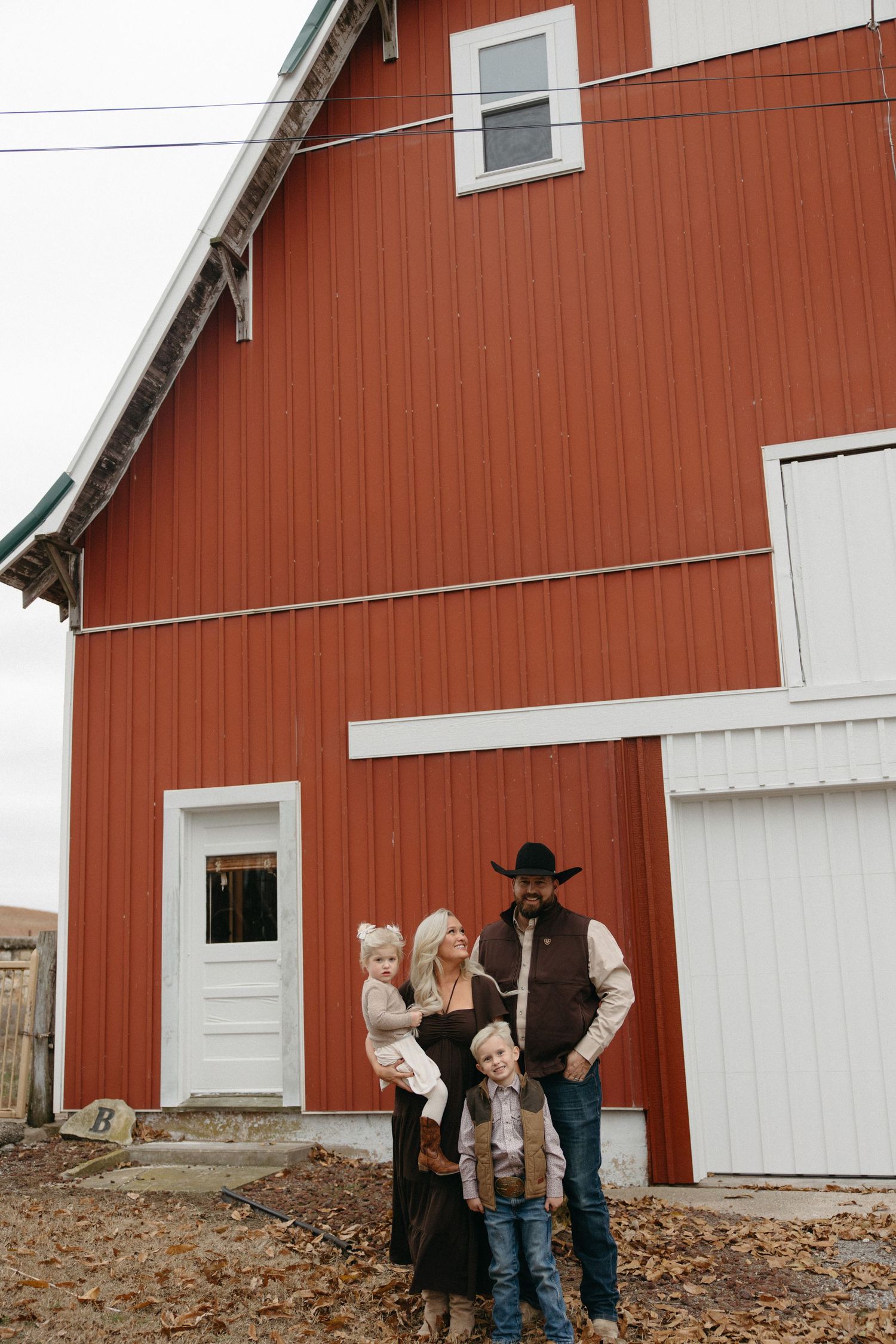 A group stands in front of a classic red barn with white trim on a fall day.