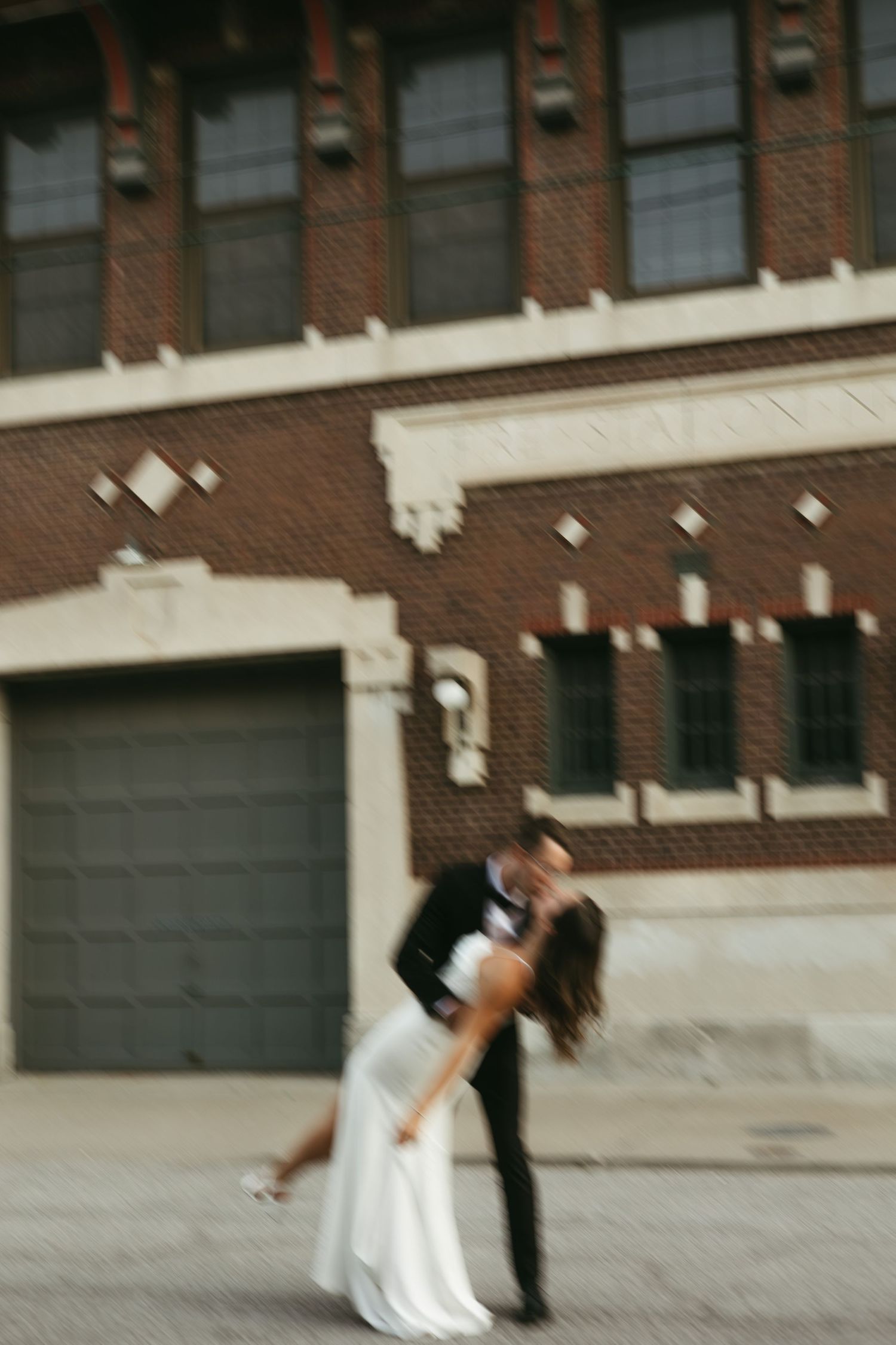 Romantic dip pose against brick building exterior during urban wedding photoshoot.