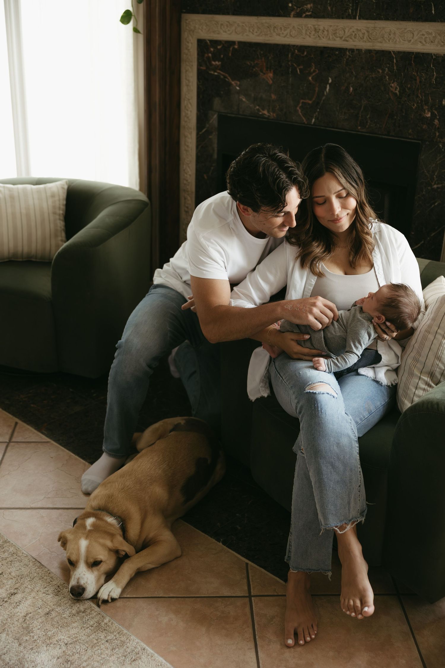 A couple sits on a couch with their brown dog while looking at something together on the floor.