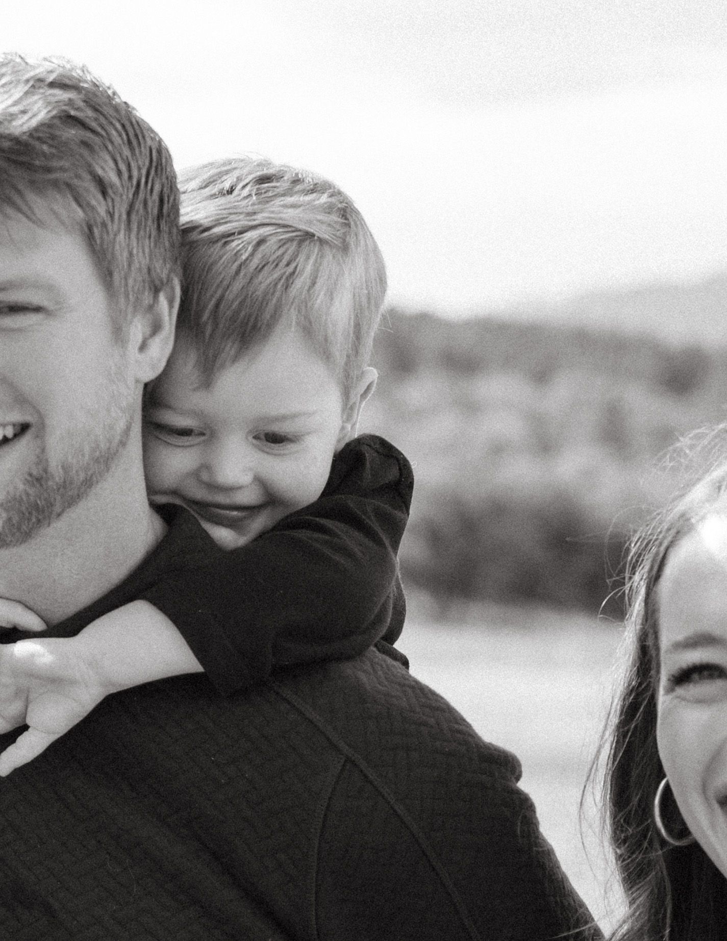 Black and white candid family portrait showing joyful expressions and close bonds in an outdoor setting.