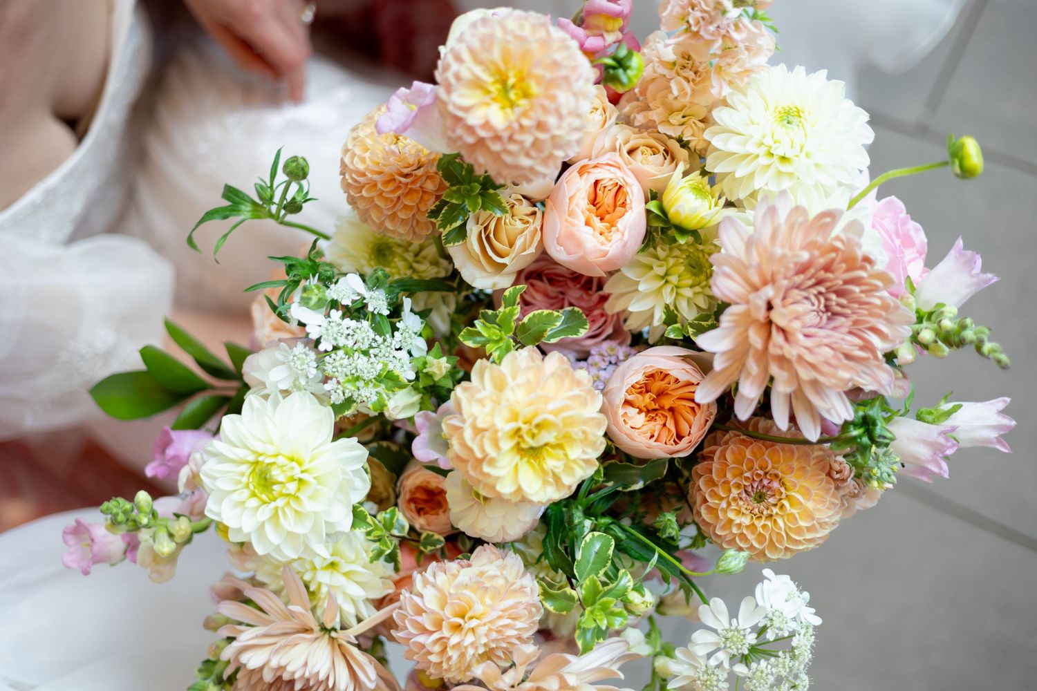 Elegant wedding bouquet featuring peach, pink and white flowers with greenery.