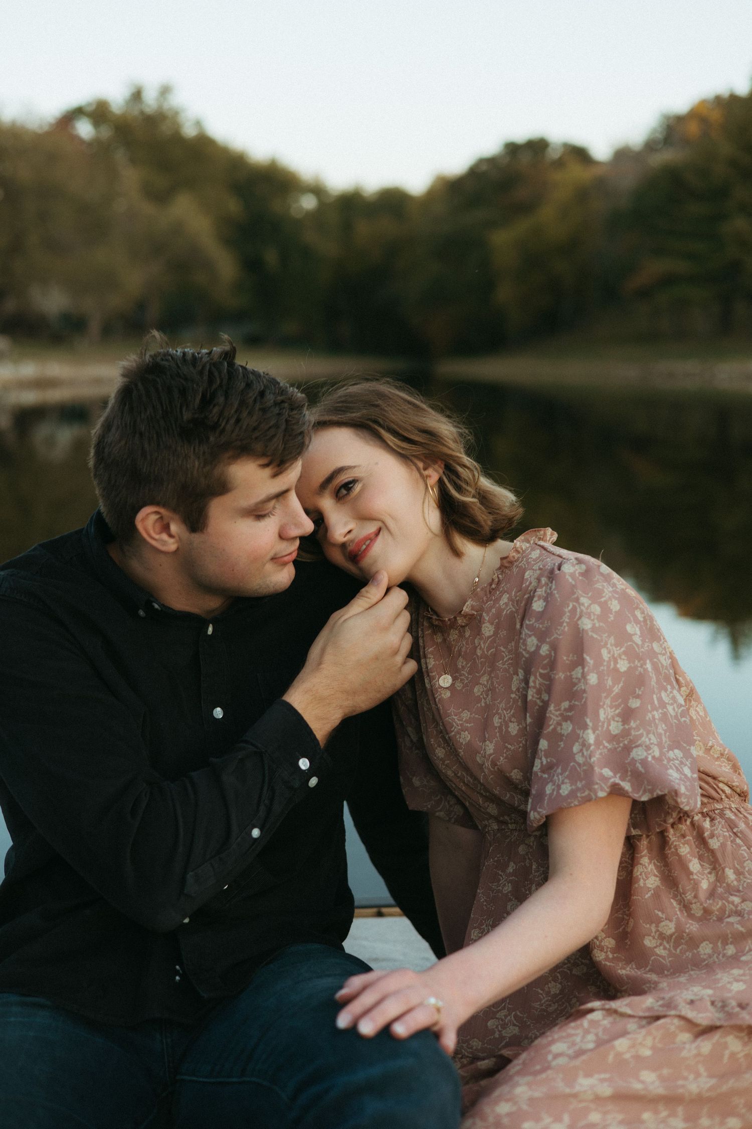 A couple shares an intimate moment by a serene lake during golden hour.