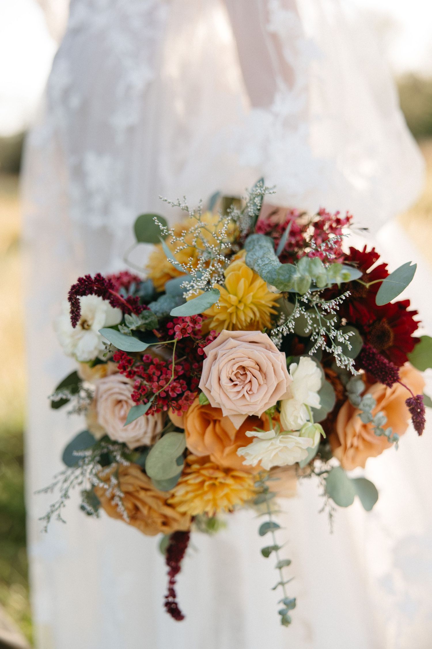 Close-up view of autumn wedding bouquet with burgundy, yellow, and blush roses mixed with eucalyptus leaves and greenery.