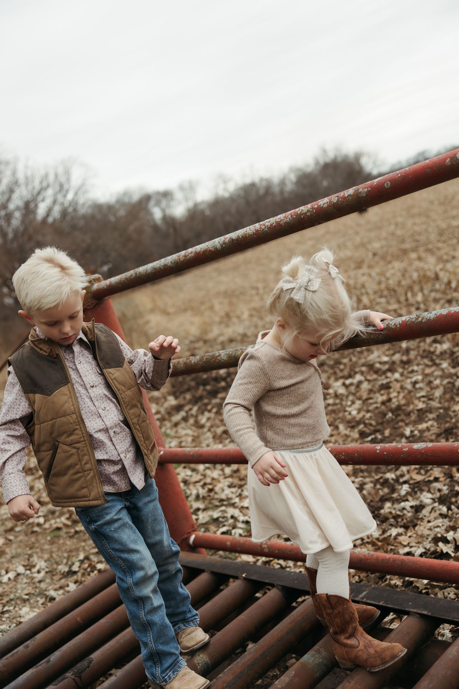 Two children play together on red metal playground equipment covered in fallen autumn leaves.