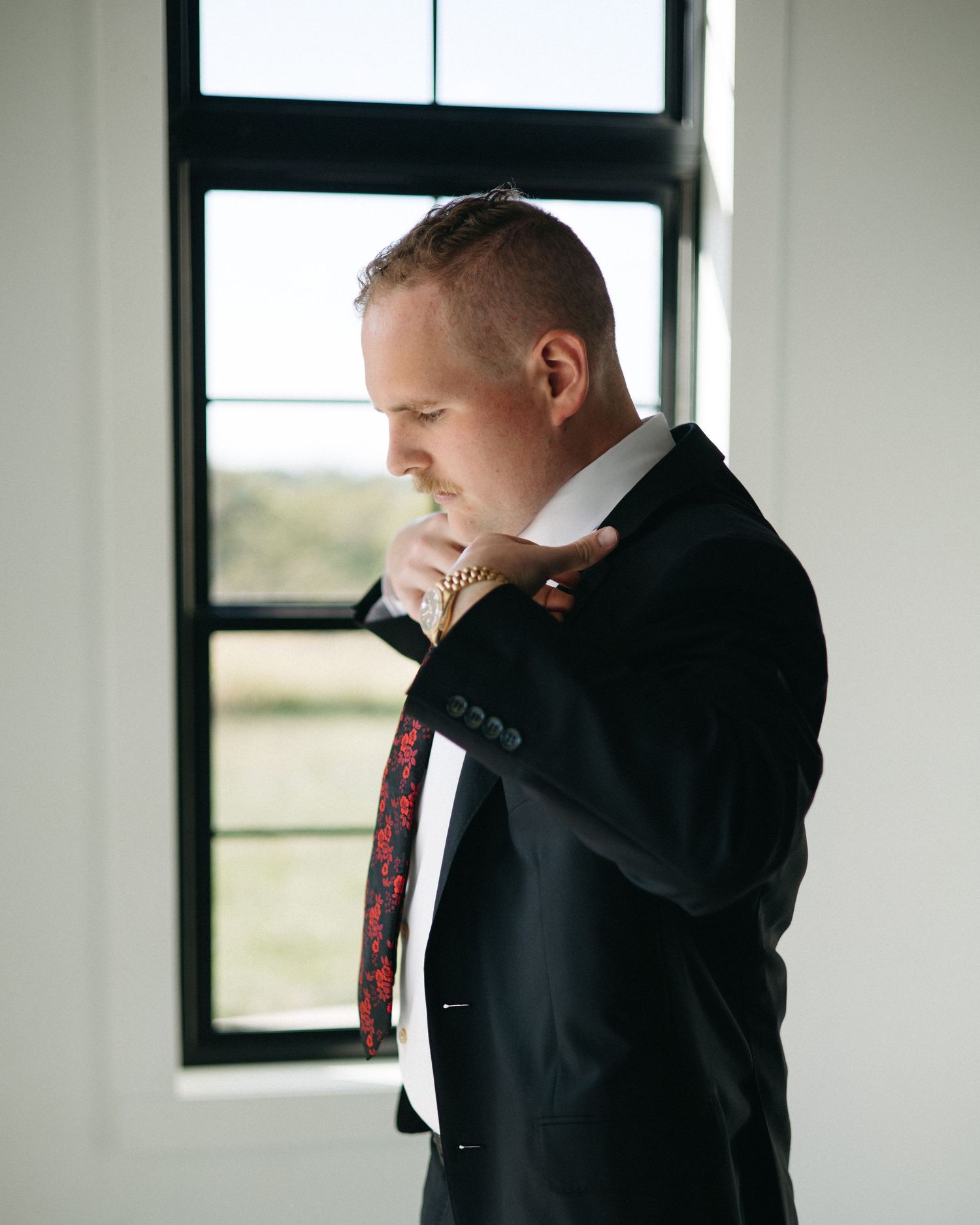 Profile view of person adjusting tie while standing by window.