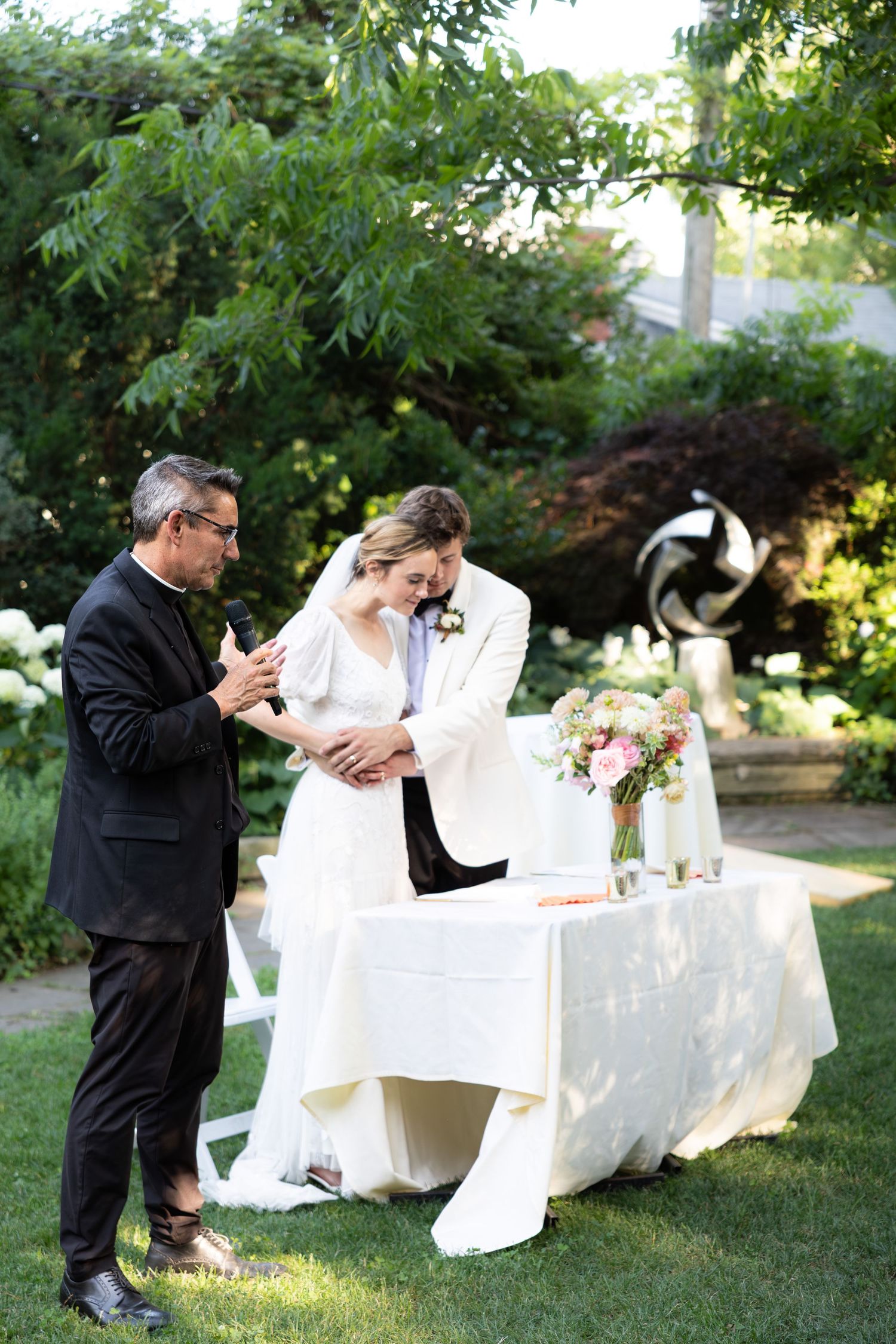 Outdoor wedding celebration with white tables and garden setting.