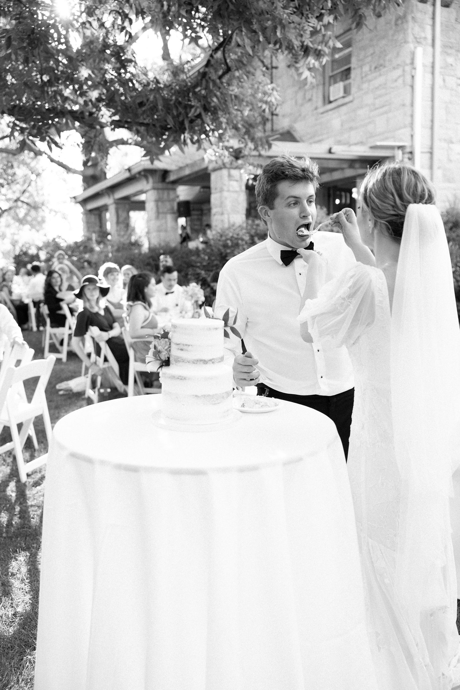 An outdoor wedding reception with guests seated at tables while a server in formal attire tends to guests.