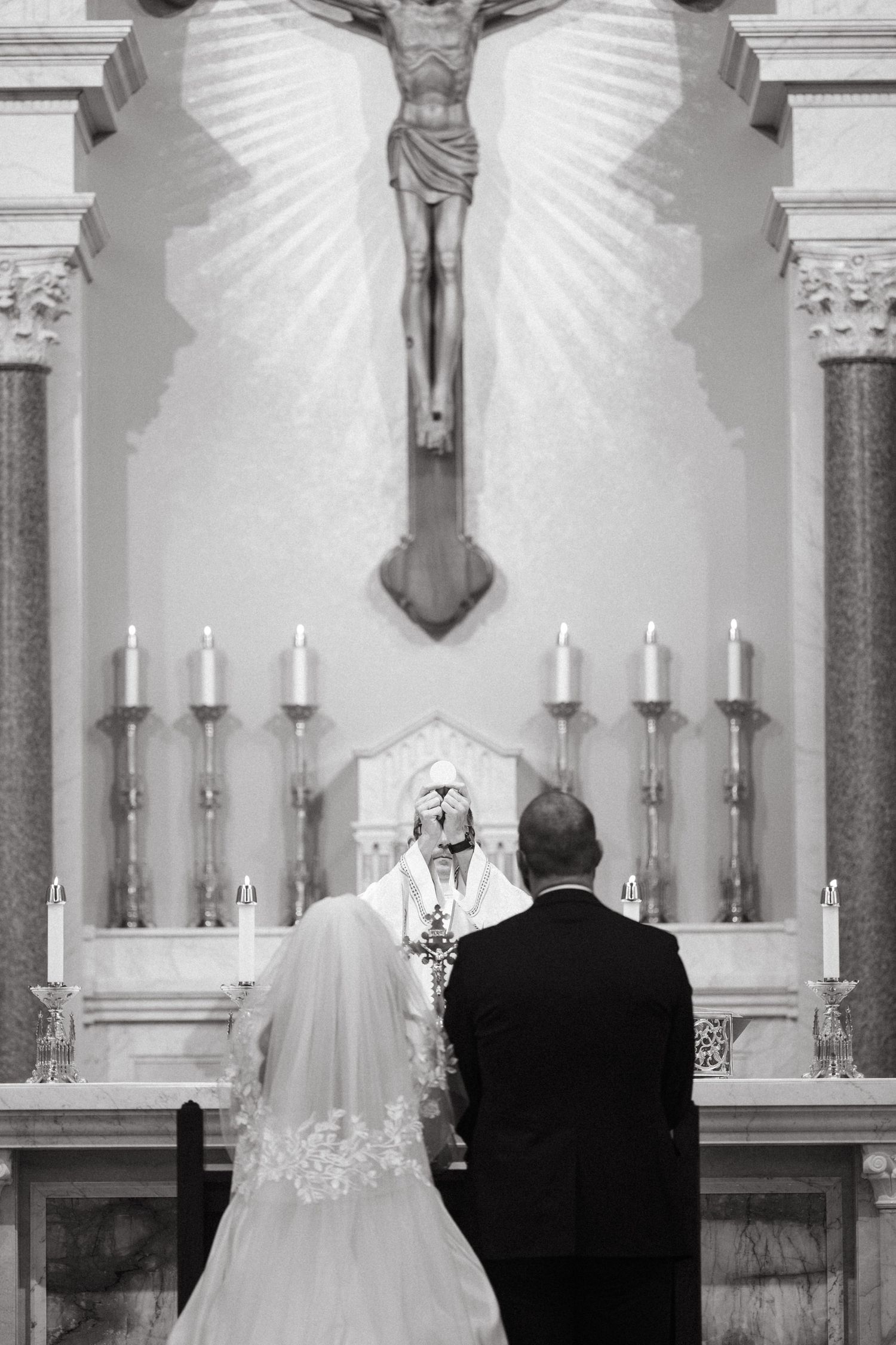 A wedding ceremony in progress at a traditional church altar with white candles and religious decor.
