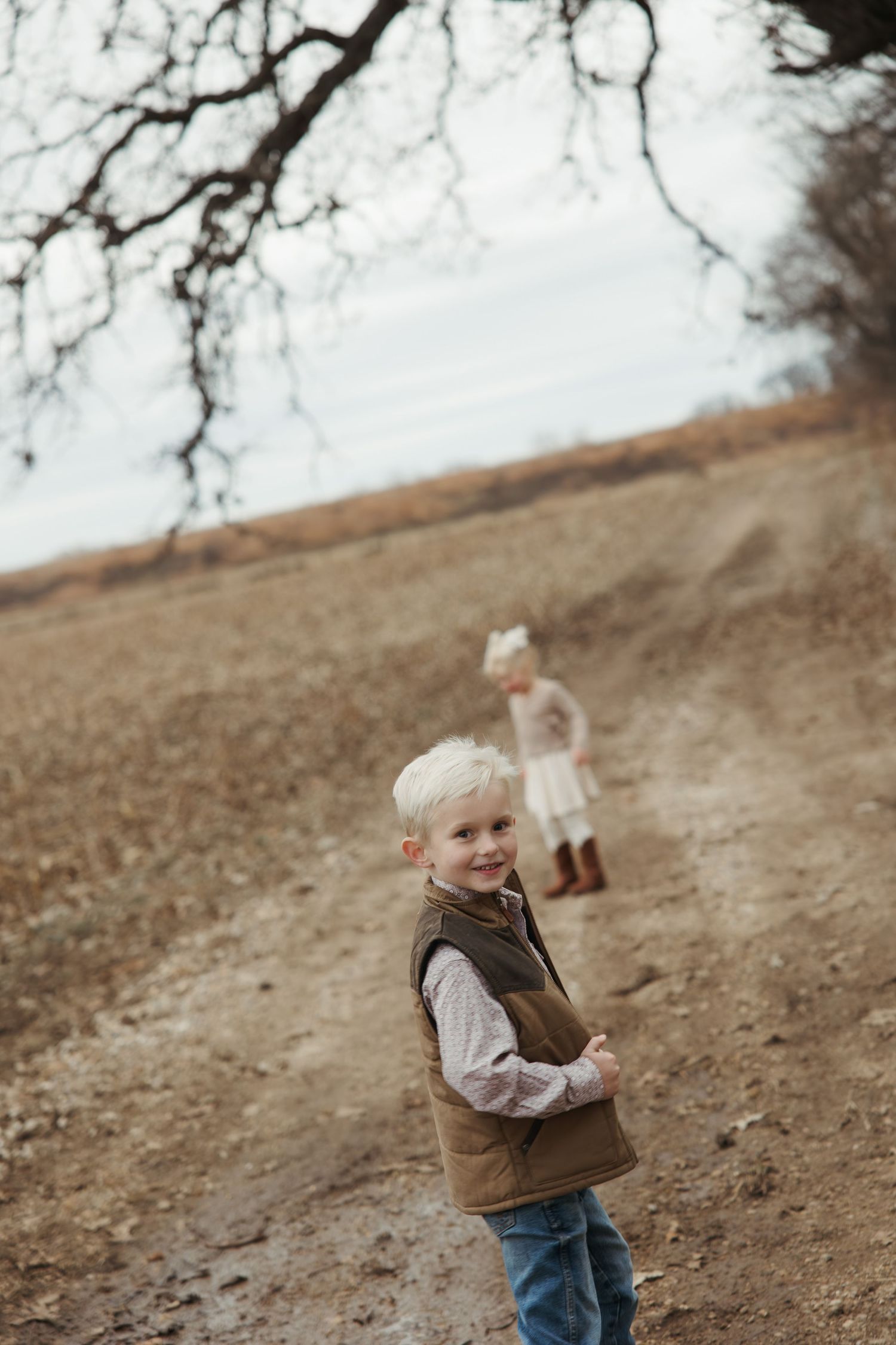 Two children playing on a dirt path along a hillside on an overcast autumn day.