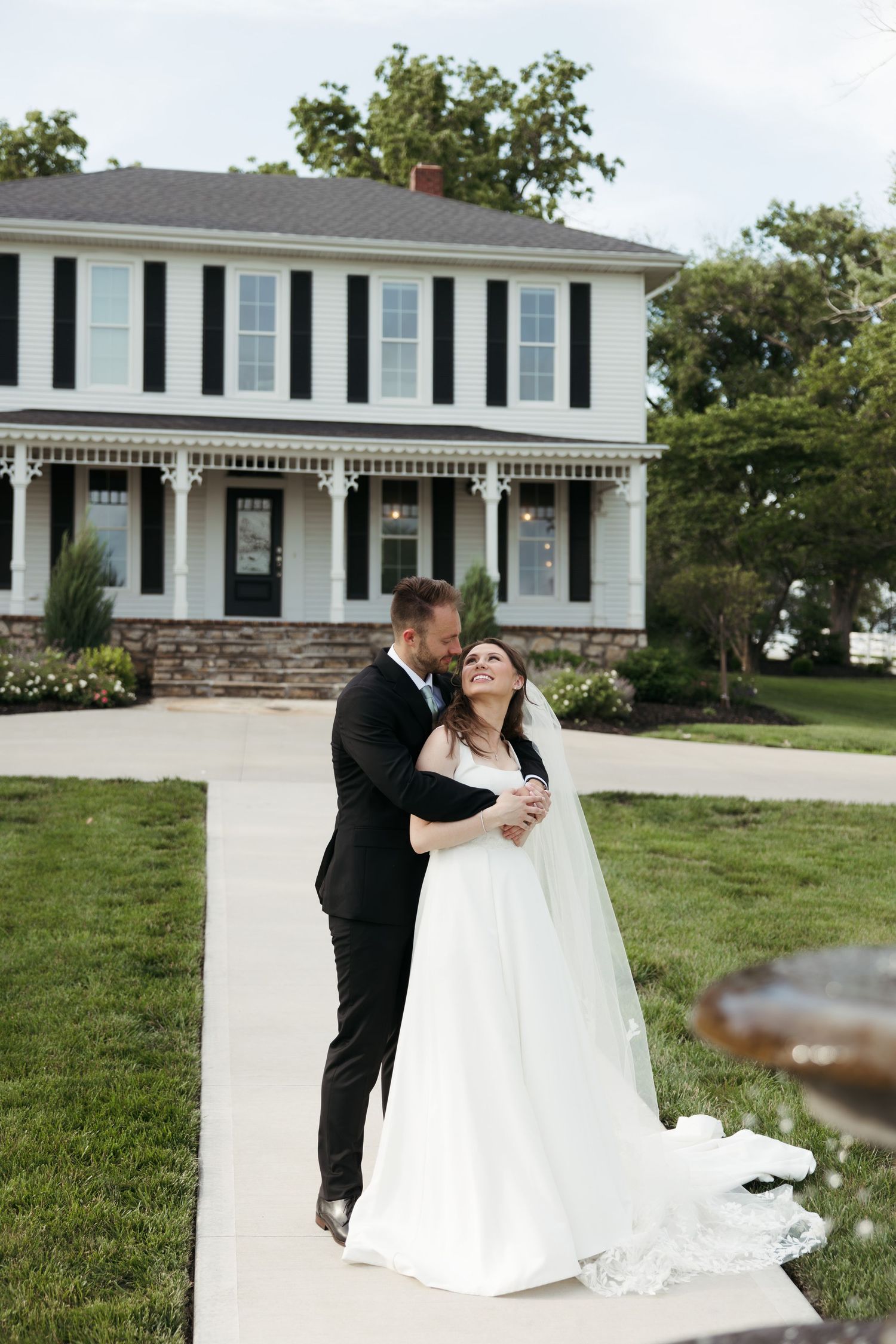 Bride and groom embracing on a pathway in front of a classic white two-story wedding venue.