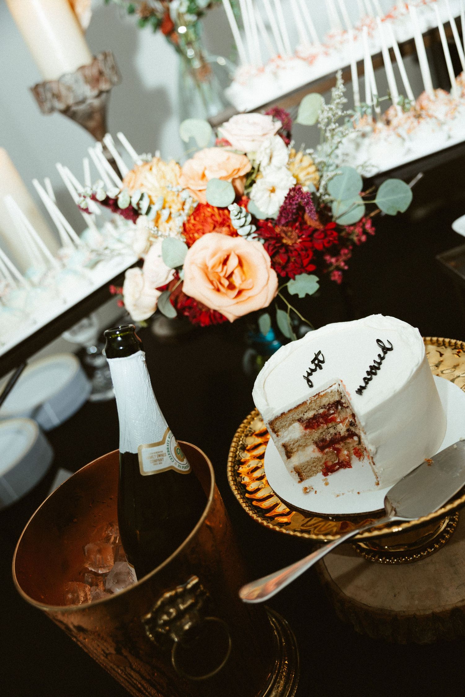 Wedding cake being cut and served on decorative plates with floral arrangements in the background.