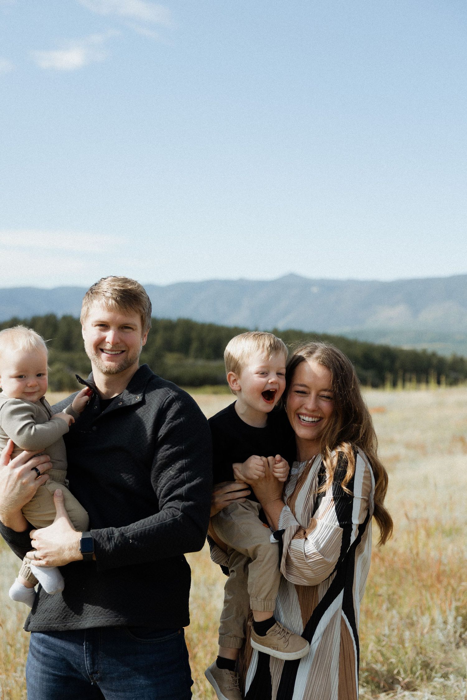 Family enjoying a candid moment together in a scenic field with mountains in the background.