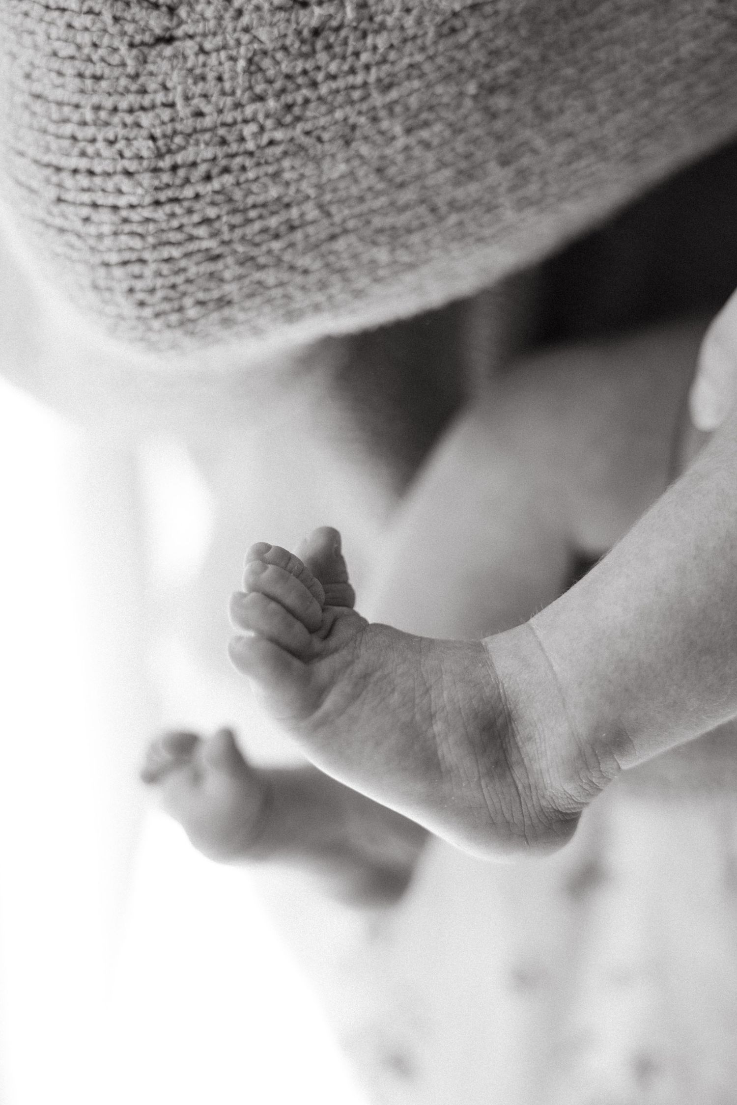 Close-up black and white photo of tiny baby feet wrapped in soft textured fabric.