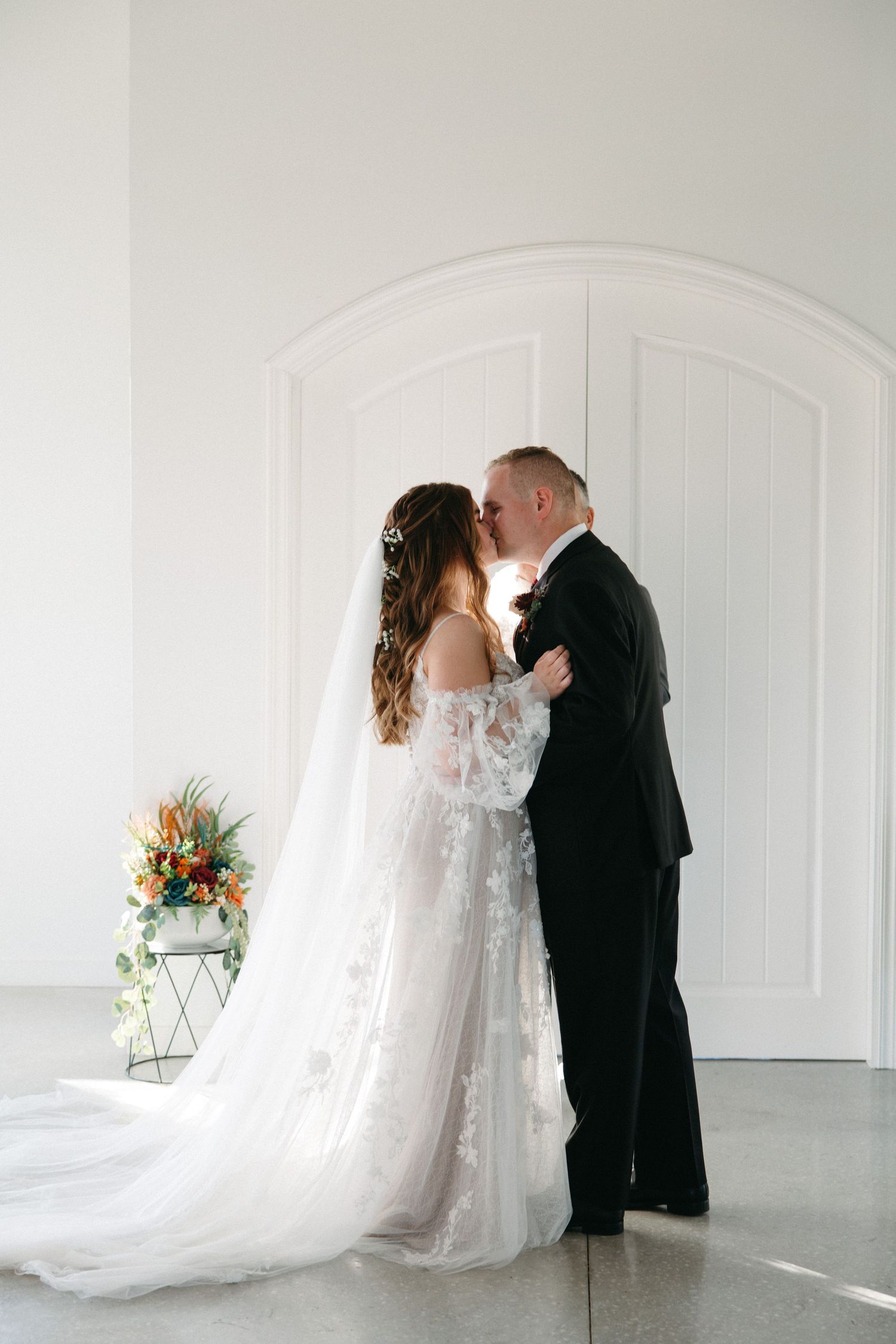 A romantic wedding couple shares intimate moments in a bright white studio space with flowing bridal veil and formal attire.