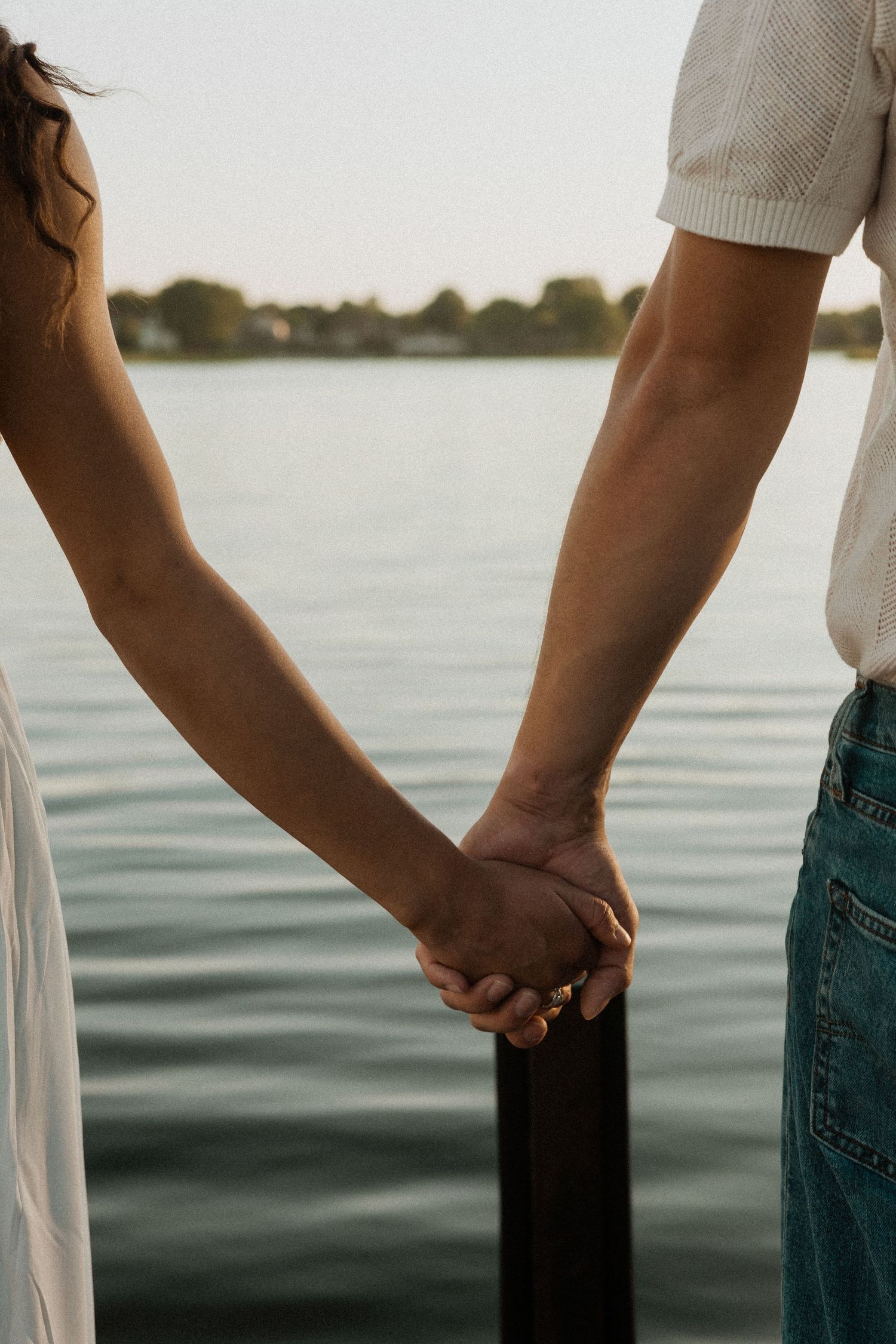 Silhouetted hands holding onto dock posts against calm water at sunset.