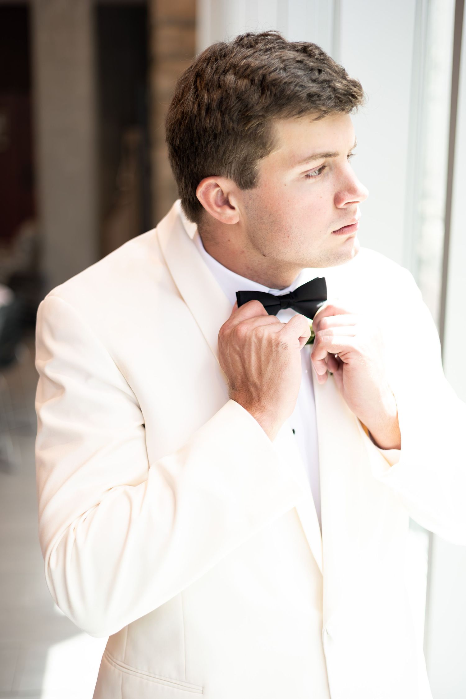 Getting ready scene showing details of a white tuxedo jacket against a bright window.