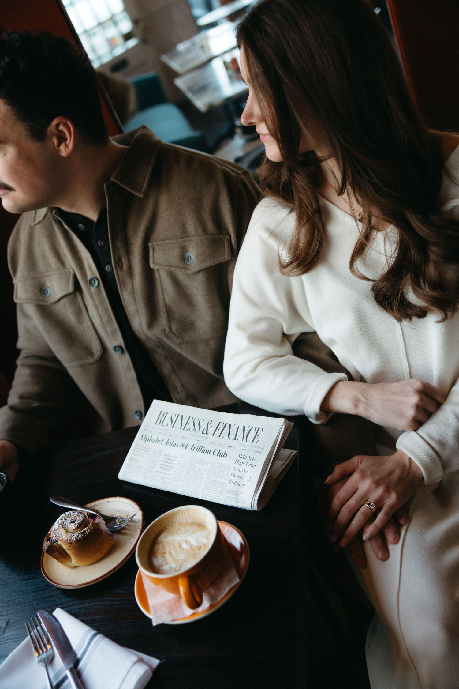 A couple shares coffee and pastries while reading together at a cozy cafe table.