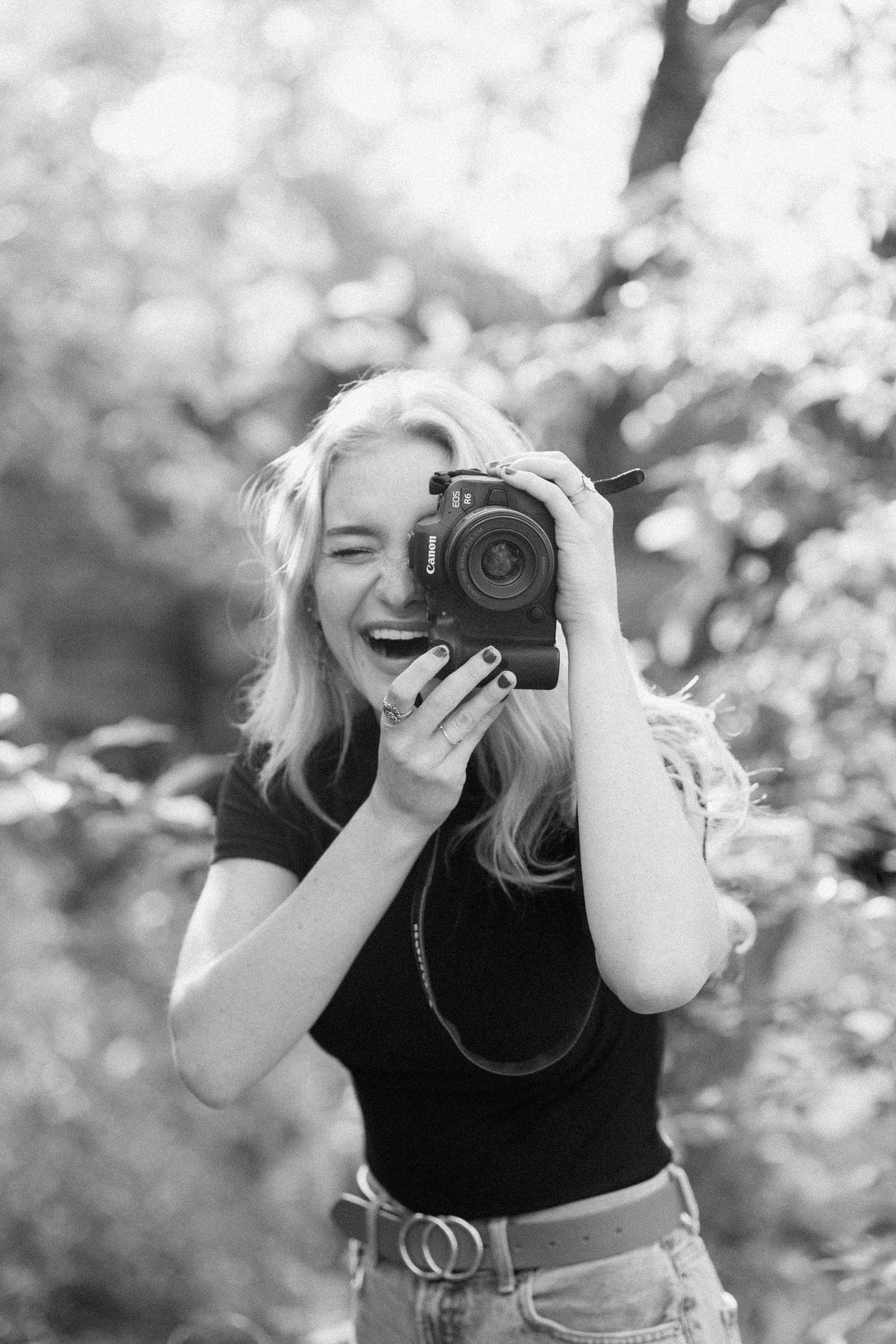Black and white photo of photographer with camera against bokeh background.