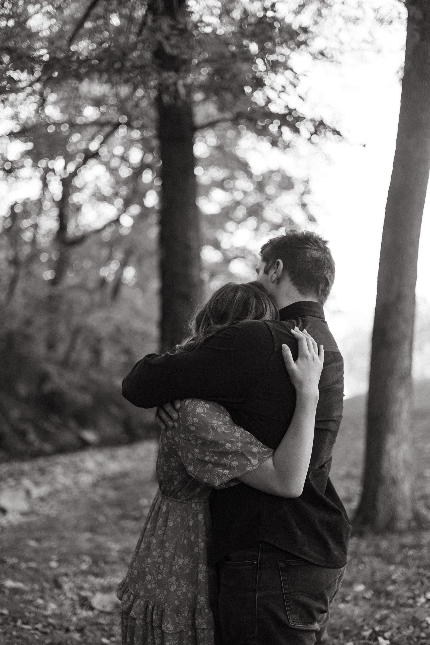 A romantic black and white photo of a couple embracing in a wooded forest setting.
