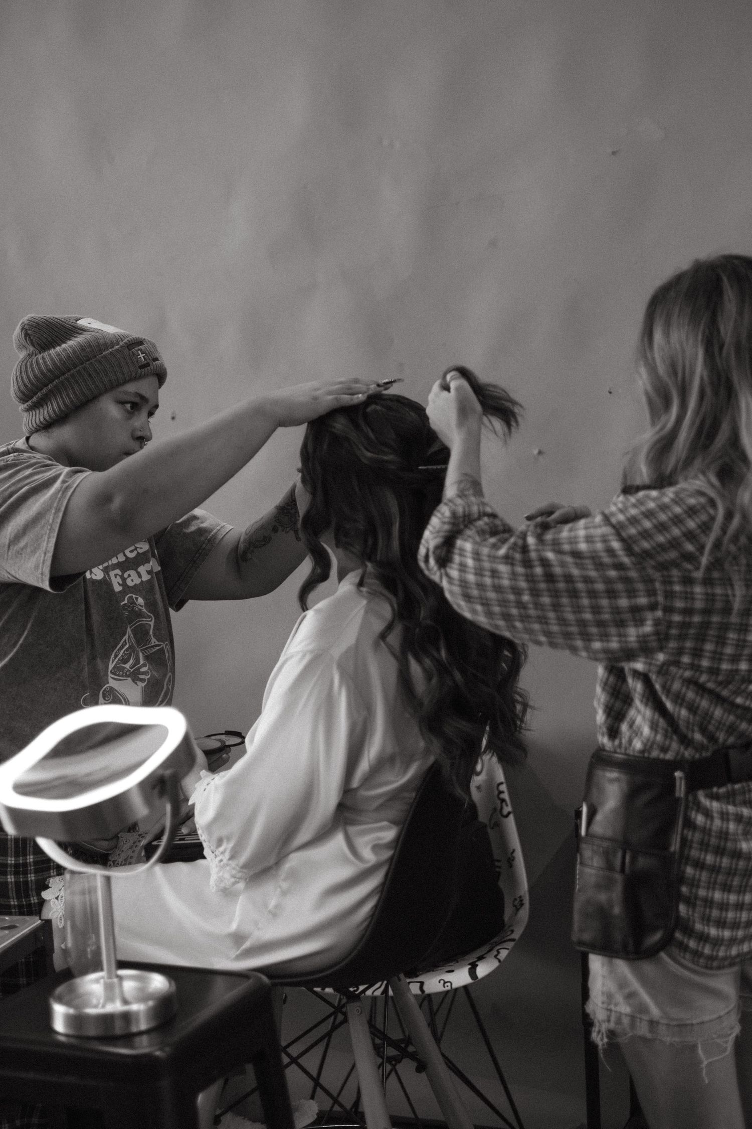 Behind the scenes shot of hairstylists working together on a client's hair with a ring light in the foreground.