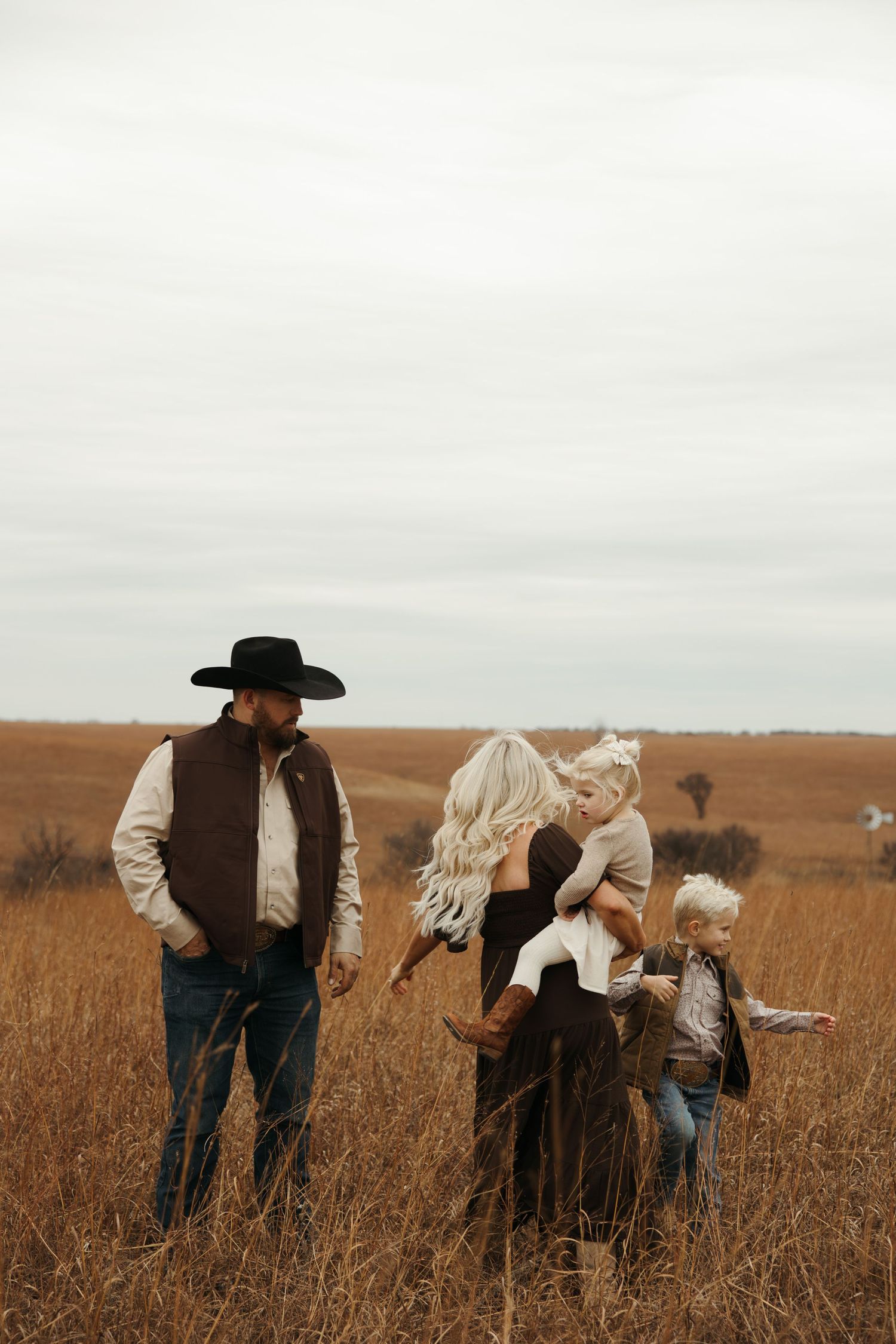 A couple in western attire embraces in a golden prairie field during an outdoor photo session.