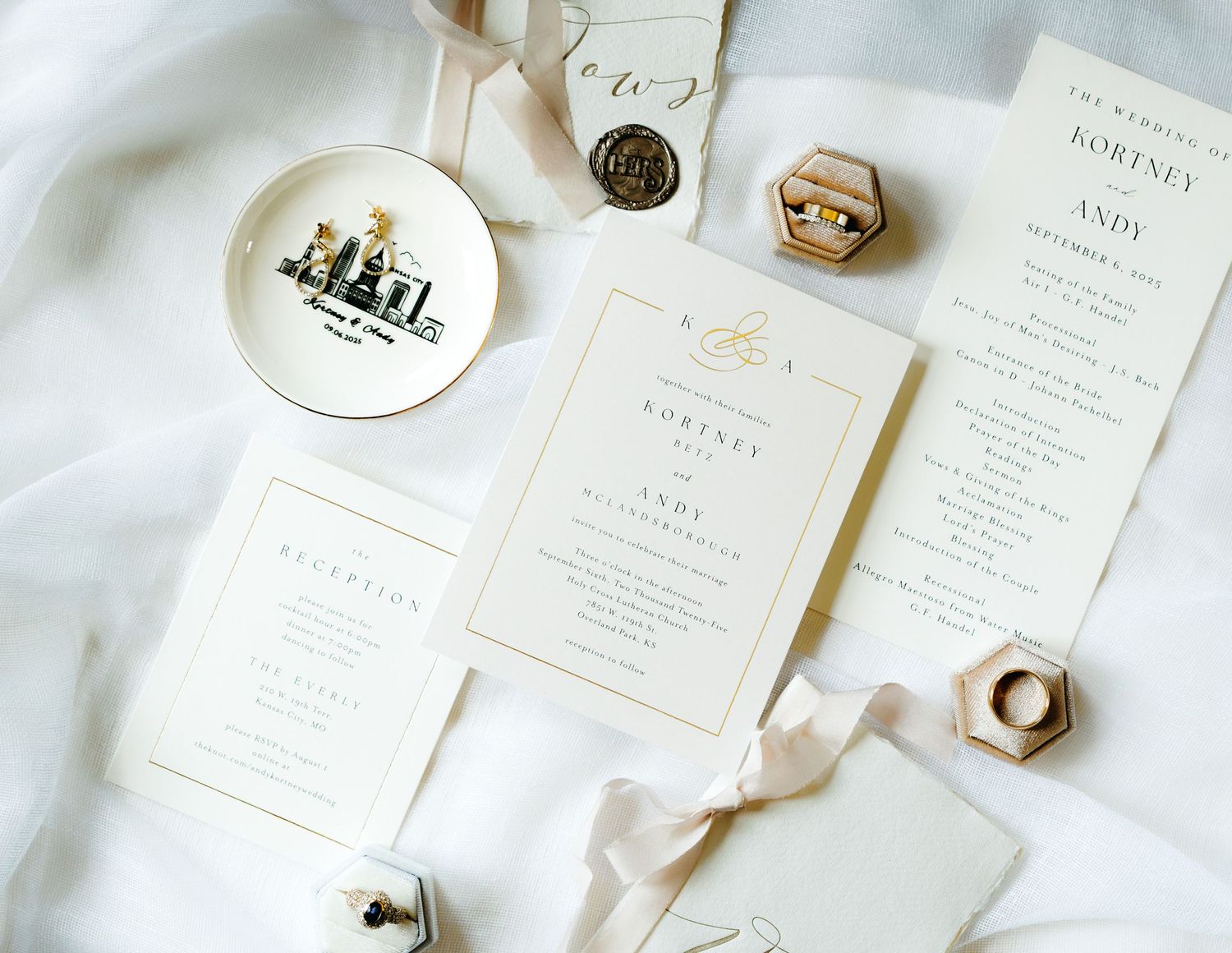 Elegant wedding invitation suite in white and gold with silk ribbons and wax seals laid out on light fabric.