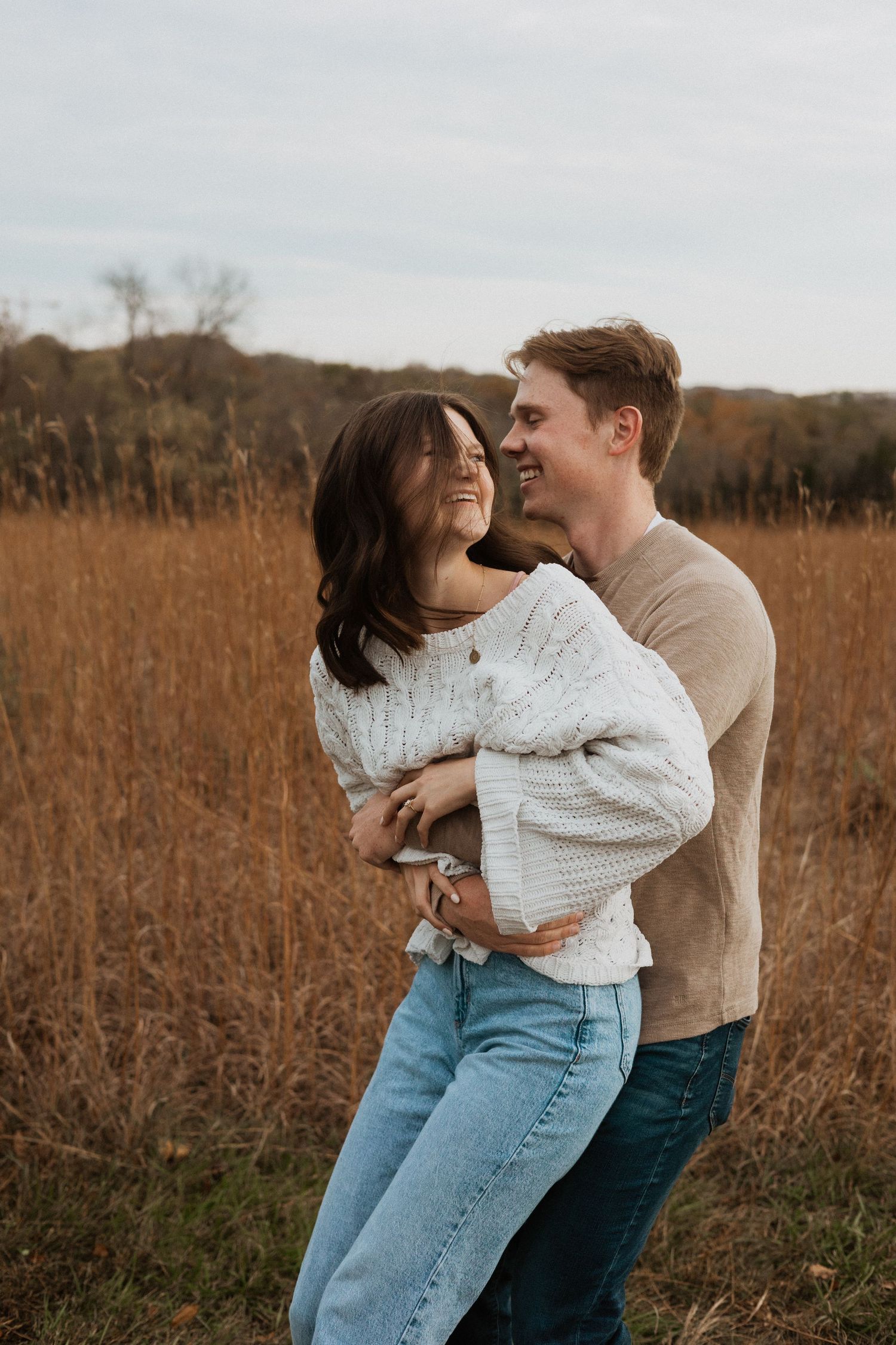 A couple shares joyful moments together in a rustic field with dried grass and autumn colors.