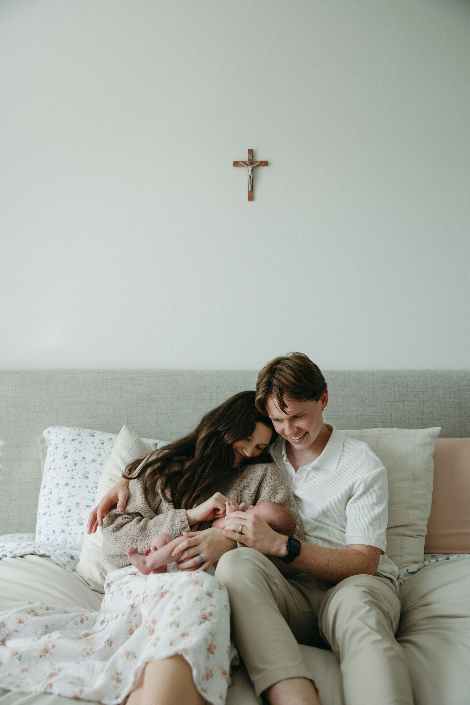 Family resting together on gray couch with small crucifix on wall.