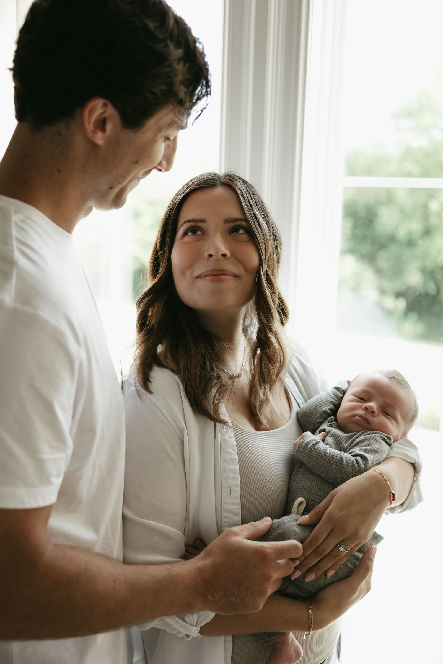 A series of intimate photos showing parents tenderly holding and caring for their newborn baby in a sunlit room.
