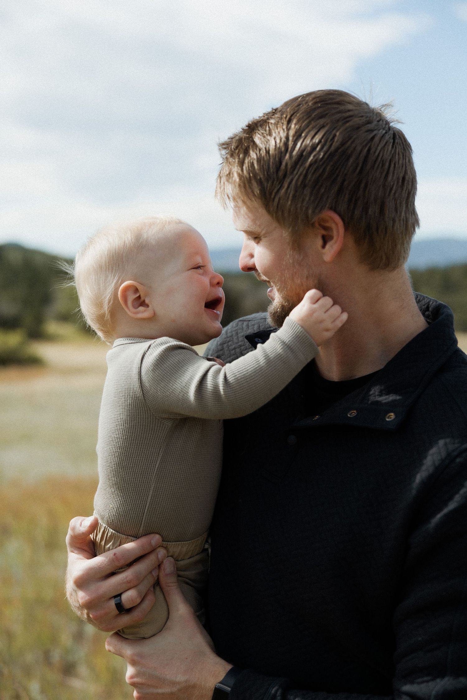 A tender moment between parent and child playing together in a grassy field on a sunny day.
